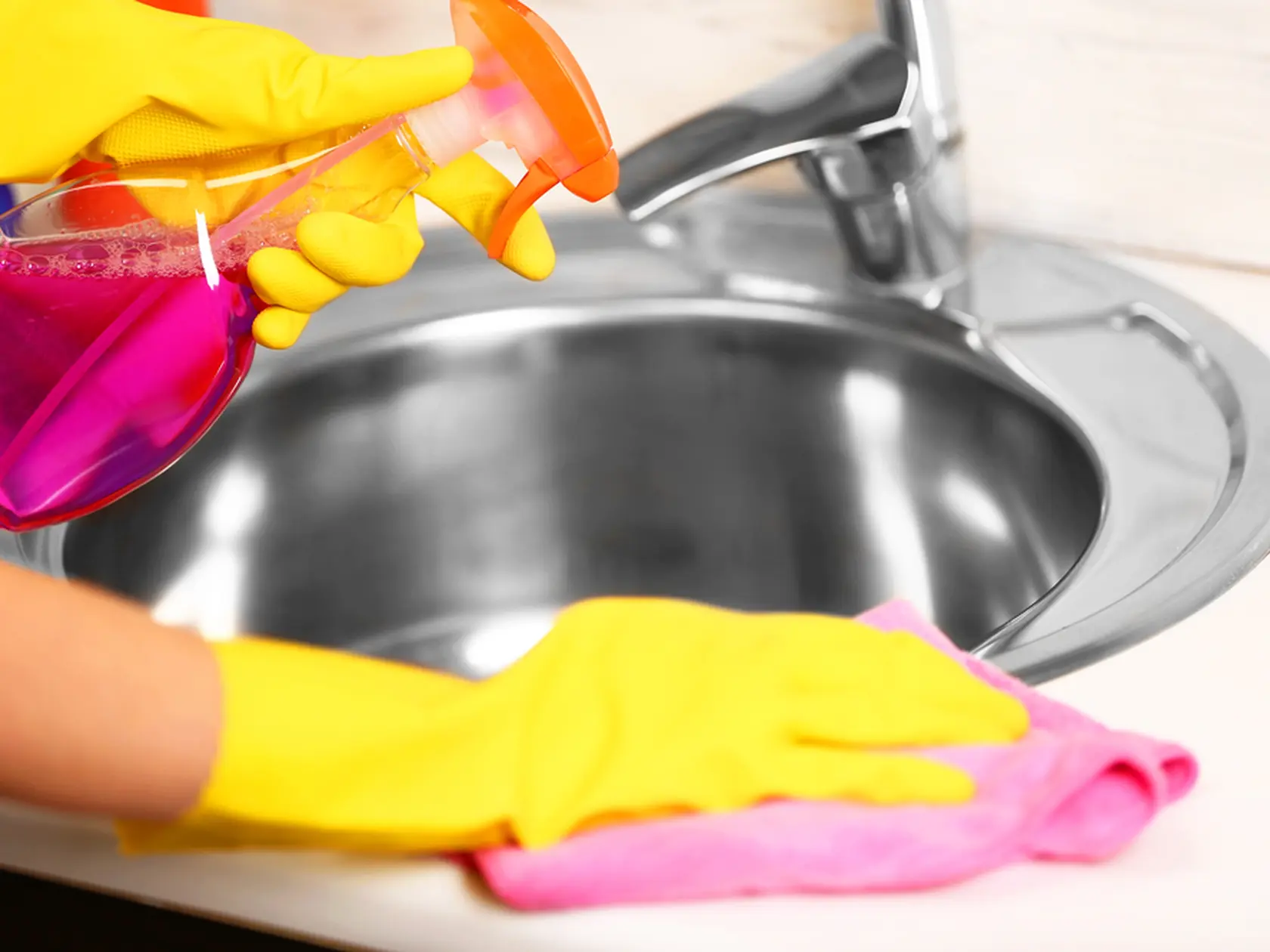 Female hands with rag and detergent spray cleaning a sink in the kitchen