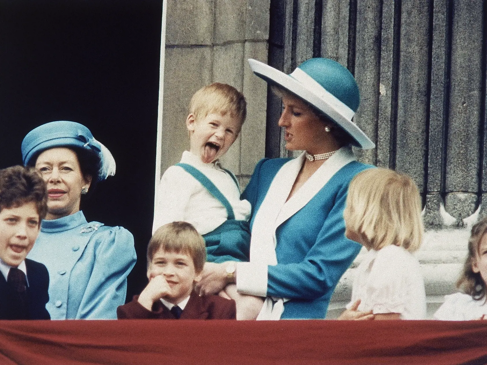 FILE - In this June 11, 1988 file photo Britain's Prince Harry sticks out his tongue for the cameras on the balcony of Buckingham Palace in London, England following the Trooping of the Colour. Princess Diana holds Harry, as a smiling Prince William sits in front, and Lady Gabriella Windsor is seen on the left. (AP Photo/Steve Holland, file)