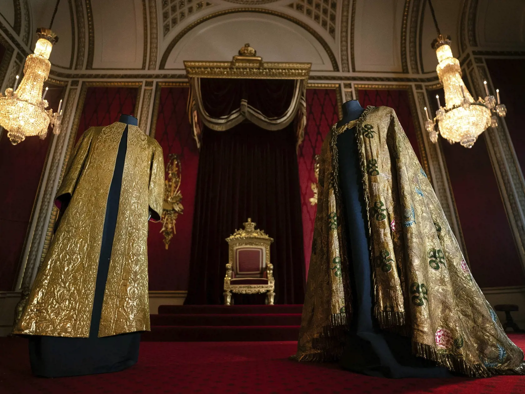 Na snímke vyšívaná zlatá tunika (vľavo) z roku 1911, ktorú bude mať na sebe oblečenú britský kráľ Charles III. počas pomazania a následne  bude mať potom na tunike ešte oblečený kráľovský plašť (vpravo) z roku 1821, v Buckinghamskom paláci 26. apríla 2023 v Londýne.