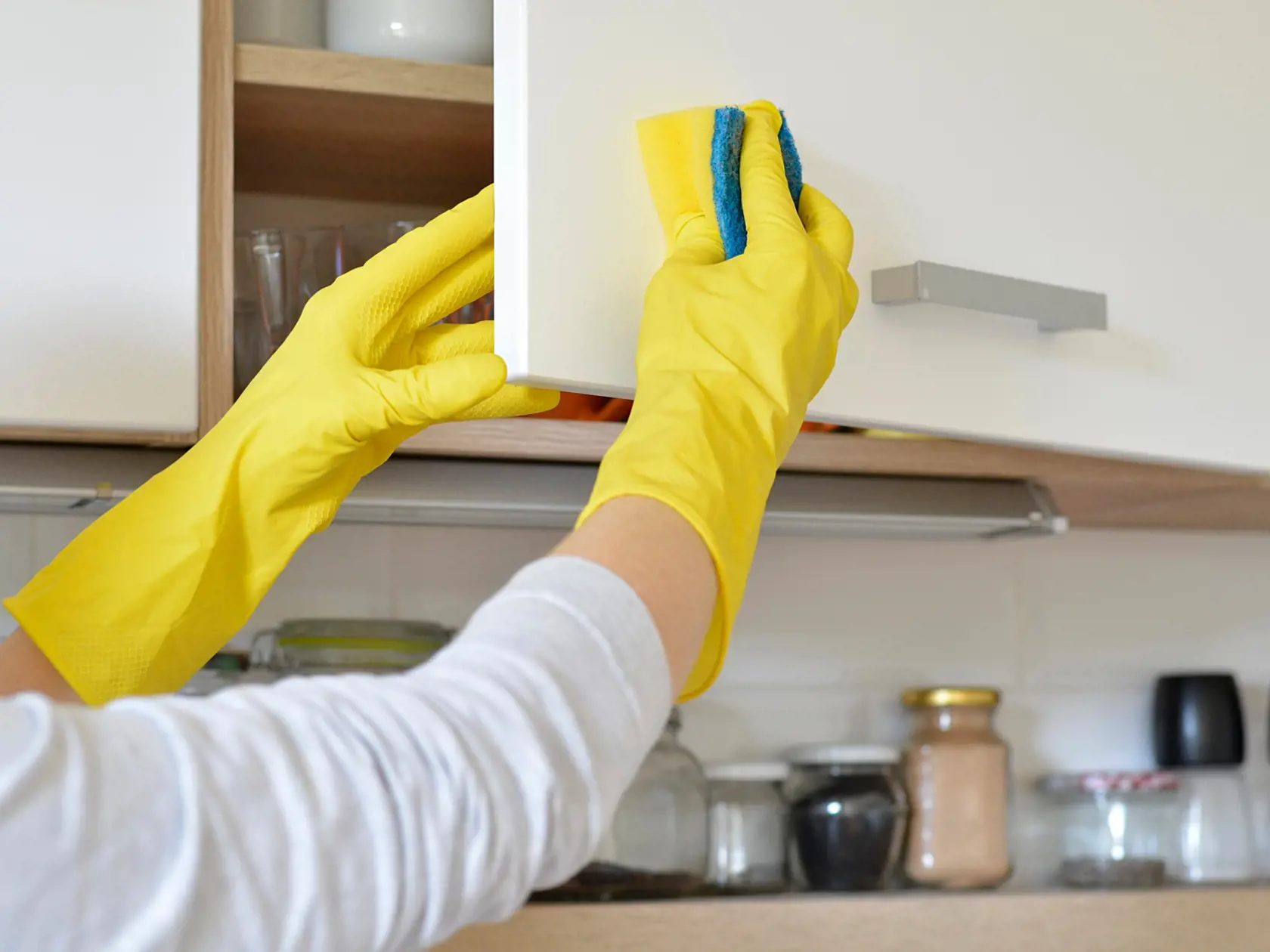woman in yellow gloves washes the door in kitchen cabinet