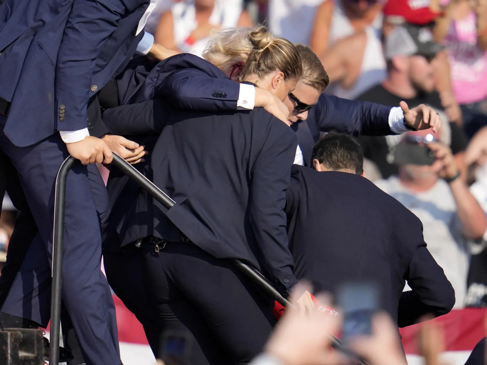 Republikánsky prezidentský kandidát Donald Trump (druhý zľava) odchádza za pomoci ochrankárov z predvolebného mítingu v meste Butler v americkom štáte Pensylvánia 13. júla 2024. Trump potvrdil, že v sobotu na mítingu v Pensylvánii ho zasiahla guľka. Tá mu prestrelila hornú časť pravého ucha.