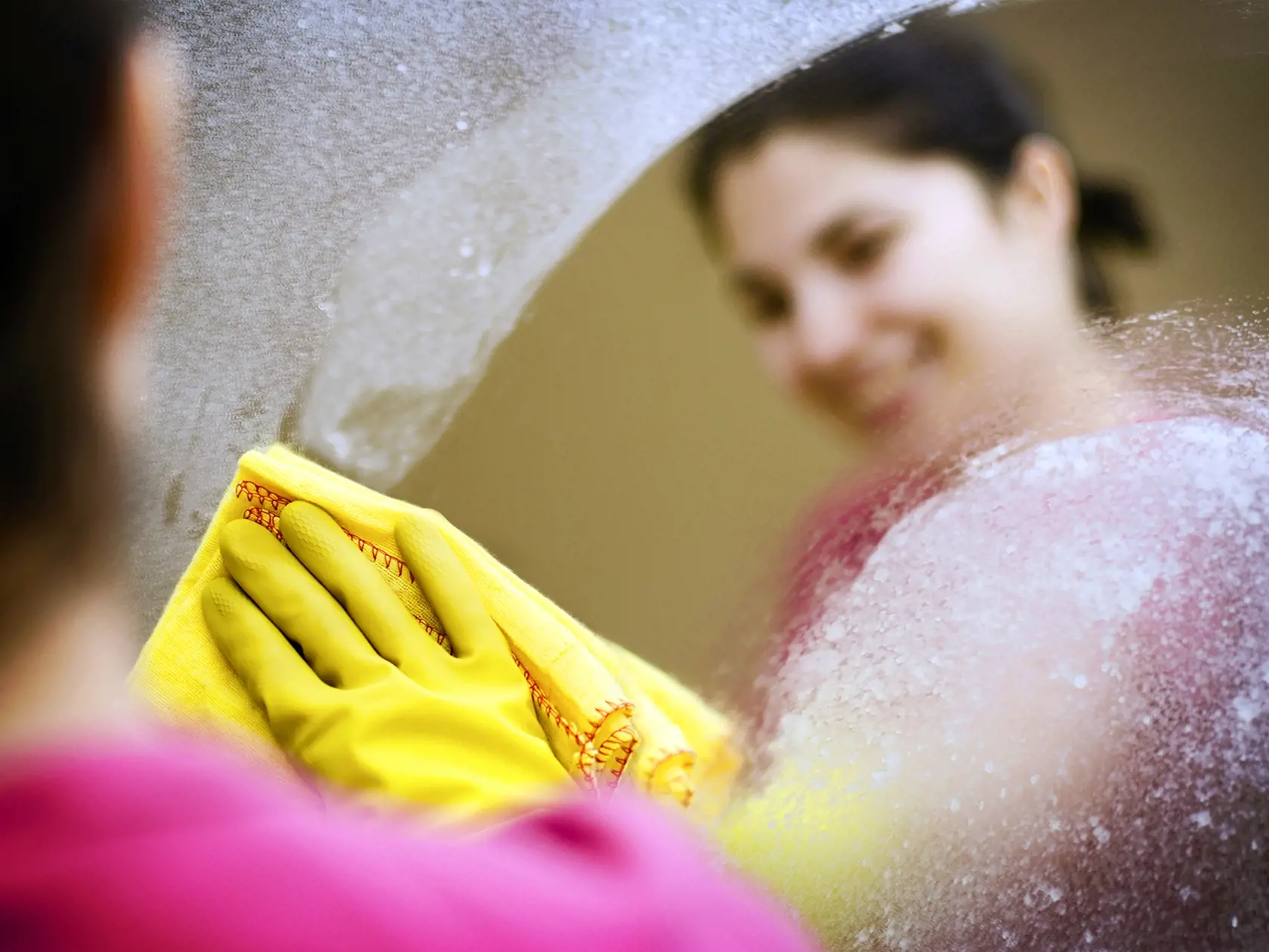 Woman smiling cleaning a mirror blurred background, soft focus intended to create interest in subject matter. 