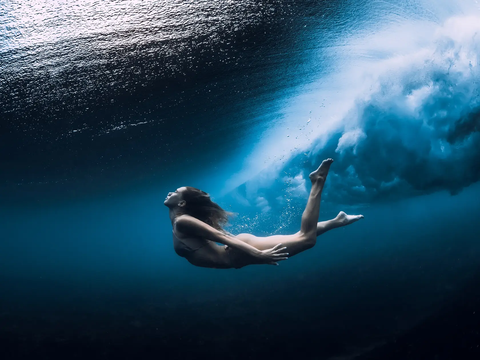 Woman swim underwater with ocean wave.