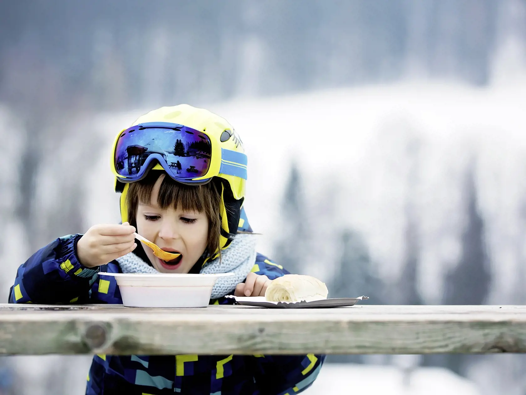 Sweet preschool child, eating soup in a restaurant on ski slope, having a break from skiing