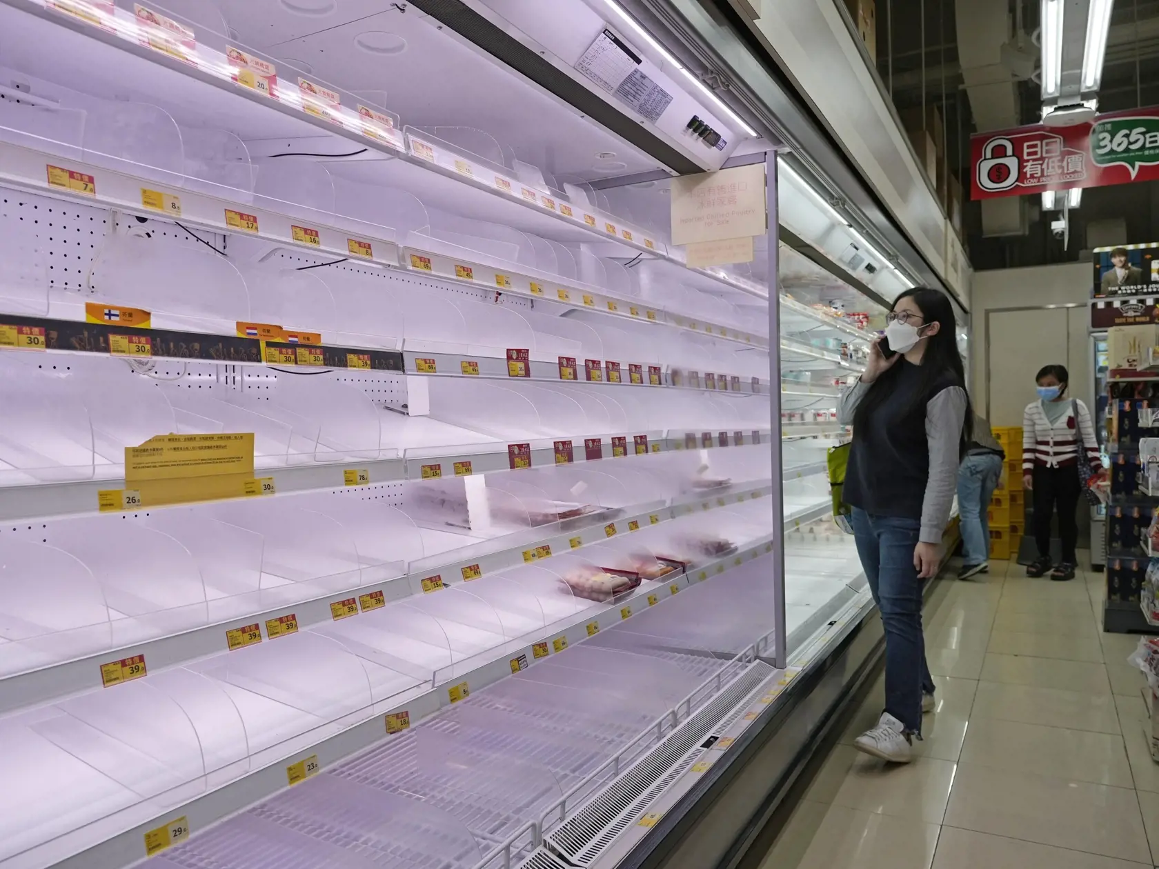 Na snímke žena stojí pred prázdnymi regálmi potravín vo vykúpenom supermarkete v Hongkongu vo štvrtok 3. marca 2022. Nové prípady nakazených koronavírusom tu stále pribúdajú a zdravotnícke úrady uviedli, že vláda môže zaviesť nové protipandemické opatrenia.