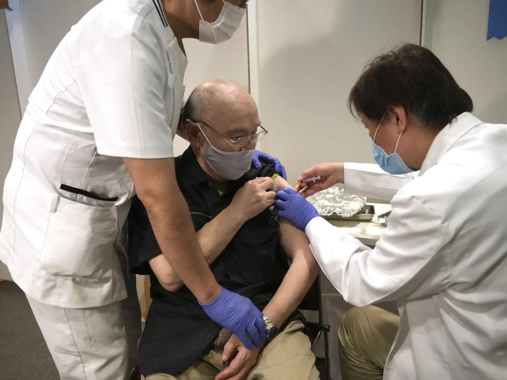 Japonec Tokumicu Aoki (uprostred) dostáva prvú dávku vakcíny proti ochoreniu COVID-19 od spoločnosti Pfizer/BioNTech počas očkovania v hromadnom očkovacom centre.