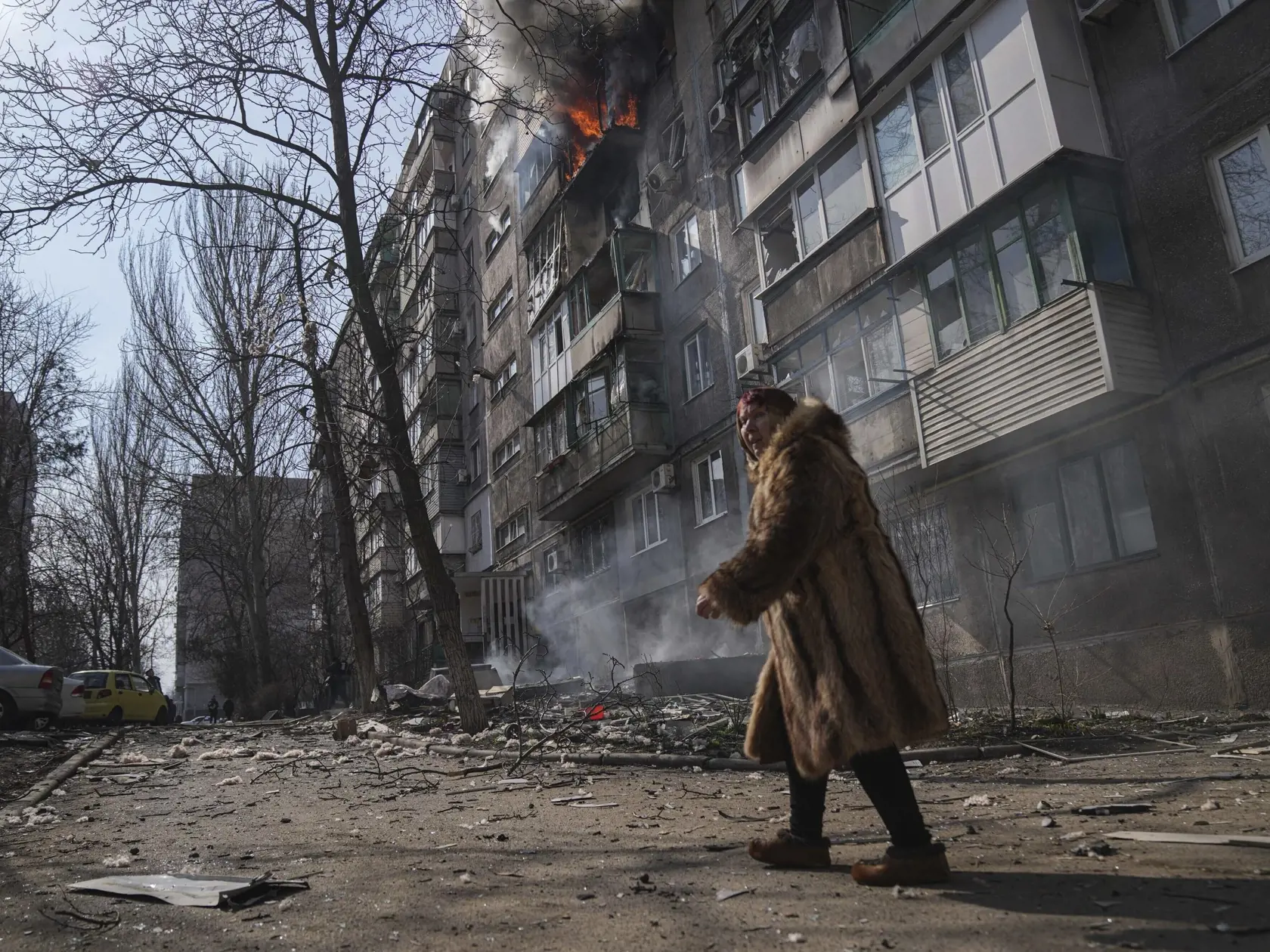 KK39 Mariupol - Žena kráča okolo horiacej budovy po ostreľovaní v prístavnom meste Mariupol na juhovýchode Ukrajiny počas 18. dňa ruskej invázie na Ukrajine v nedeľu 13. marca 2022. TASR/AP