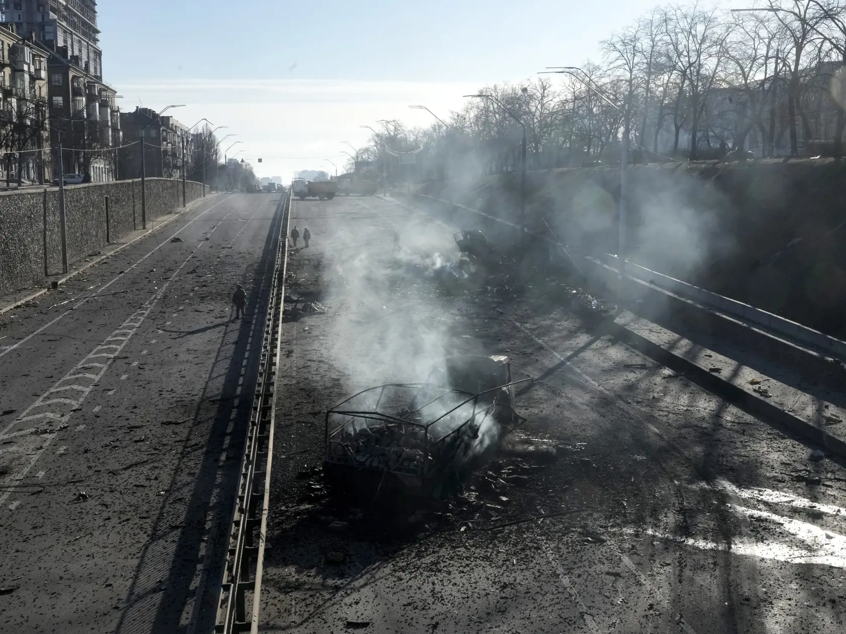KK22 Kyjev - Ukrajinskí vojaci kráčajú okolo trosiek horiacich vojenských vozidiel 26. februára 2022
