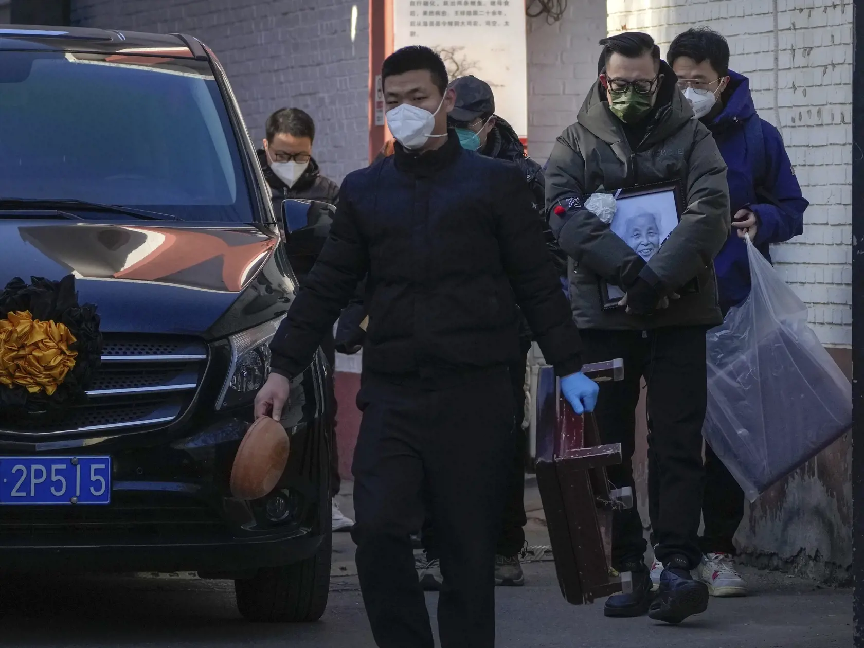 Rodinný príslušník s fotografiou zosnulého príbuzného kráča vedľa vozidla prevážajúceho telo pred klinikou 19. decembra 2022 v Pekingu. Čína hlásila v pondelok prvé dve úmrtia na ochorenie COVID-19, odkedy tamojšia vláda zrušila tzv. politiku nulovej tolerancie koronavírusu a prijala rozsiahle uvoľnenie opatrení.