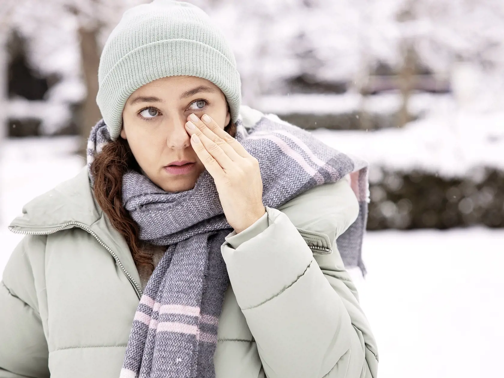 Young woman having itching eyes health problem. Sick woman in winter snow touching her sensitive eye