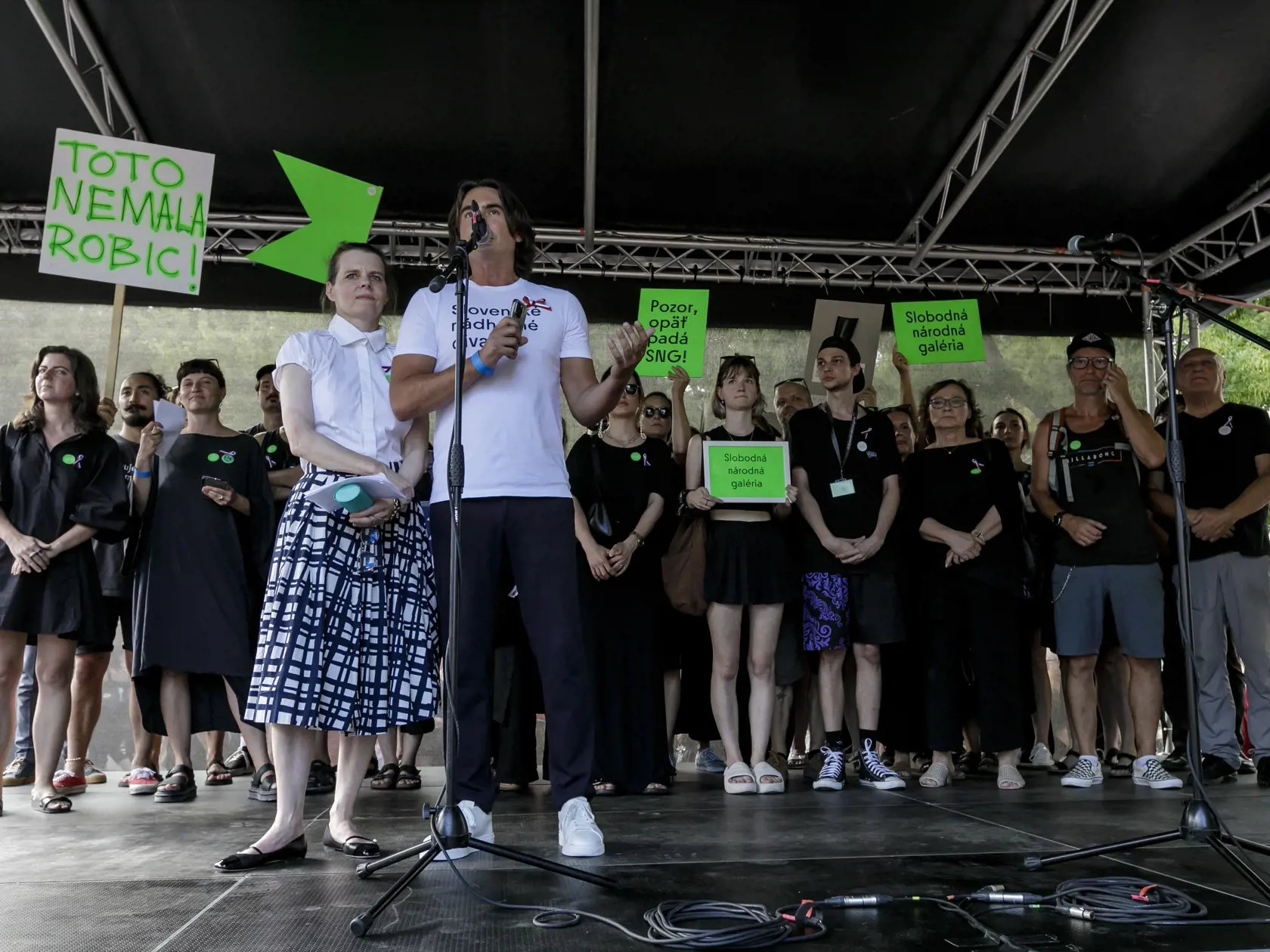 Na snímke zľava odvolaná generálna riaditeľka Slovenskej národnej galérie (SNG) Alexandra Kusá a odvolaný generálny riaditeľ Slovenského národného divadla (SND) Matej Drlička stoja na pódiu počas protestného zhromaždenia kultúrnej obce a verejnosti pred Ministerstvom kultúry na Námestí SNP v Bratislave v pondelok 12. augusta 2024. Na proteste vystúpili zástupcovia rôznych kultúrnych inštitúcií a umeleckých oblastí a organizátori prečítali spoločné vyhlásenie s požiadavkami. Protest organizátori 