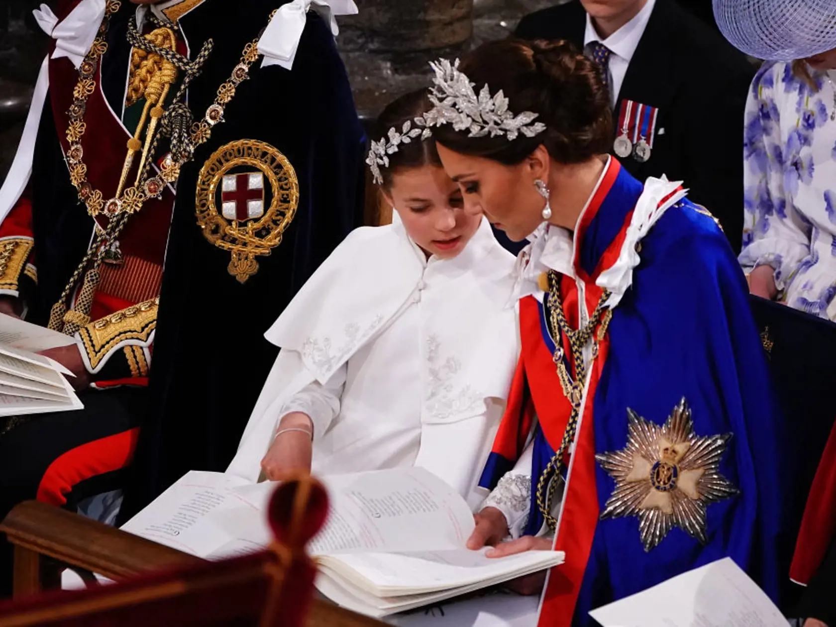 Princezná Kate mala na sebe tradičný ceremoniálny plášť. Pod ním slonovinové šaty od Alexandra McQueena a 3D čelenku, rovnako tak aj jej dcéra, princezná Charlotte.
