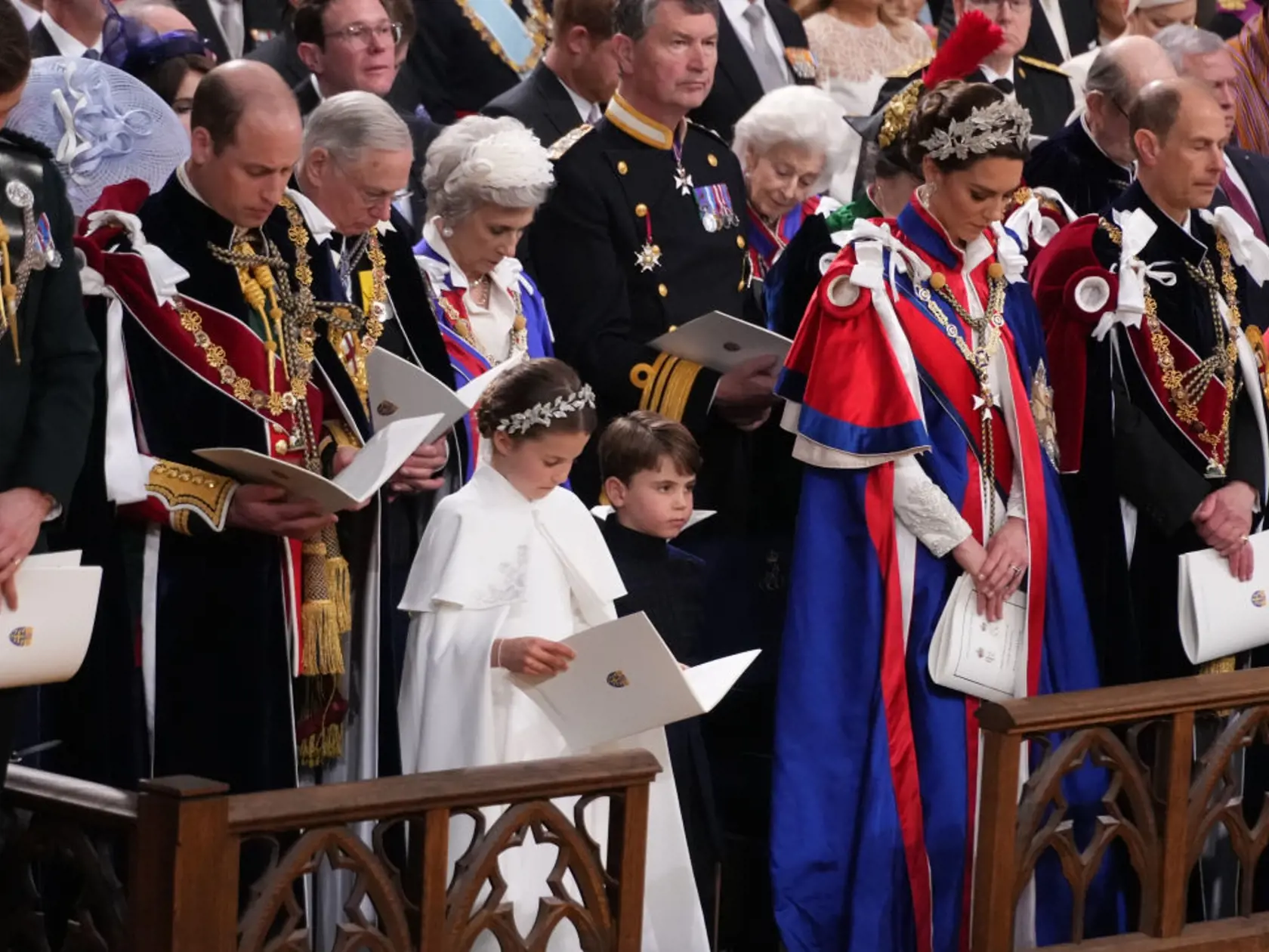 Princezná Kate mala na sebe tradičný ceremoniálny plášť. Pod ním slonovinové šaty od Alexandra McQueena a 3D čelenku, rovnako tak aj jej dcéra, princezná Charlotte.
