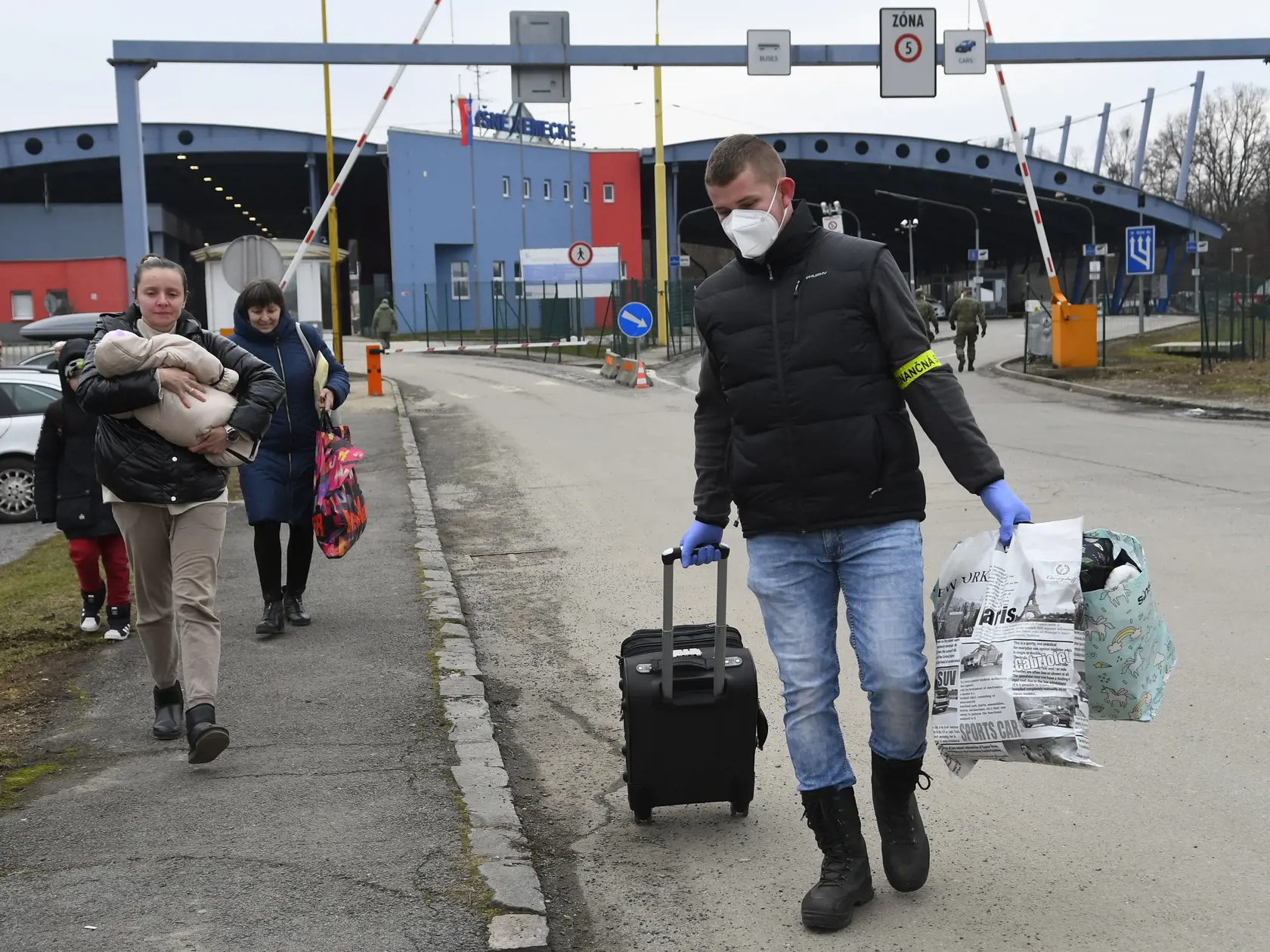 Utečenci z Ukrajiny prechádzajú cez hraničný priechod vo Vyšnom Nemeckom, vpravo im pomáha príslušník Finančnej správy SR. Vyšné Nemecké, 25. februára 2022. FOTO TASR - Milan Kapusta