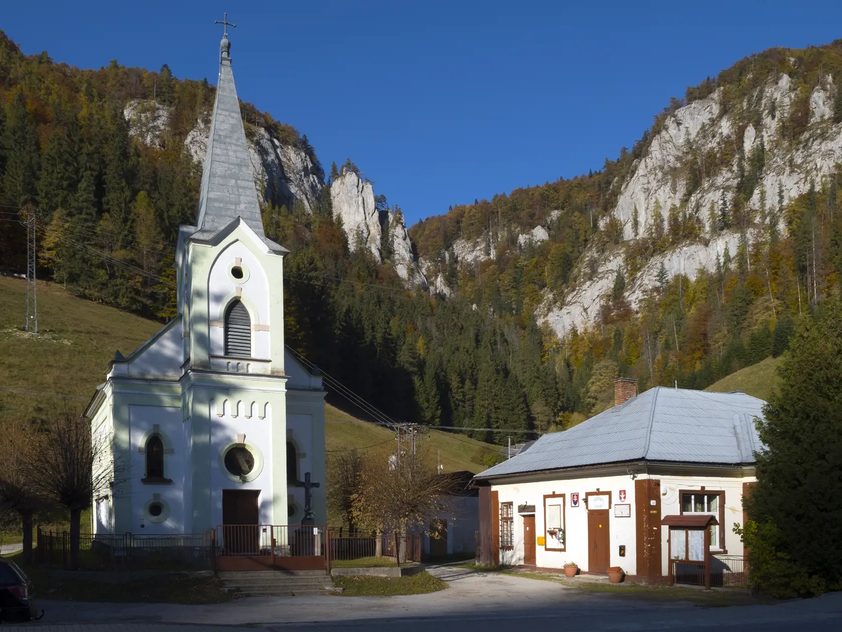 Na snímke kostol a obecný úrad v obci Stratená, okres Rožňava, v južnej časti Slovenského raja. Hore vľavo sú Sokolie skaly a vpravo vrch Marčeková. Roklinou medzi skalami vedie turistický chodník na vyhliadkový vrch Havrania skala.
