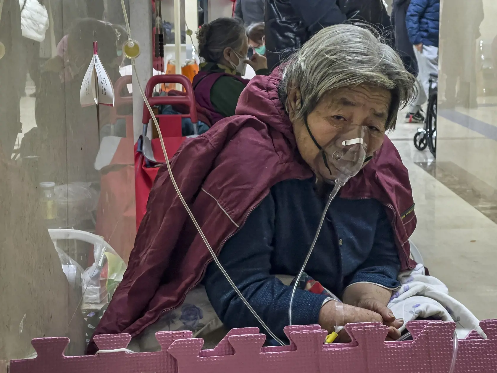 Staršia žena s kyslíkovou maskou na tvári dostáva infúziu na chodbe pohotovosti v Pekingu vo štvrtok 5. januára 2023. Pacienti, väčšinou starší ľudia, ležia na nosidlách na chodbách nemocníc alebo sedia s kyslíkovými maskami na invalidných vozíkoch počas prudkého nárastu počtu prípadov ochorenia COVID-19.