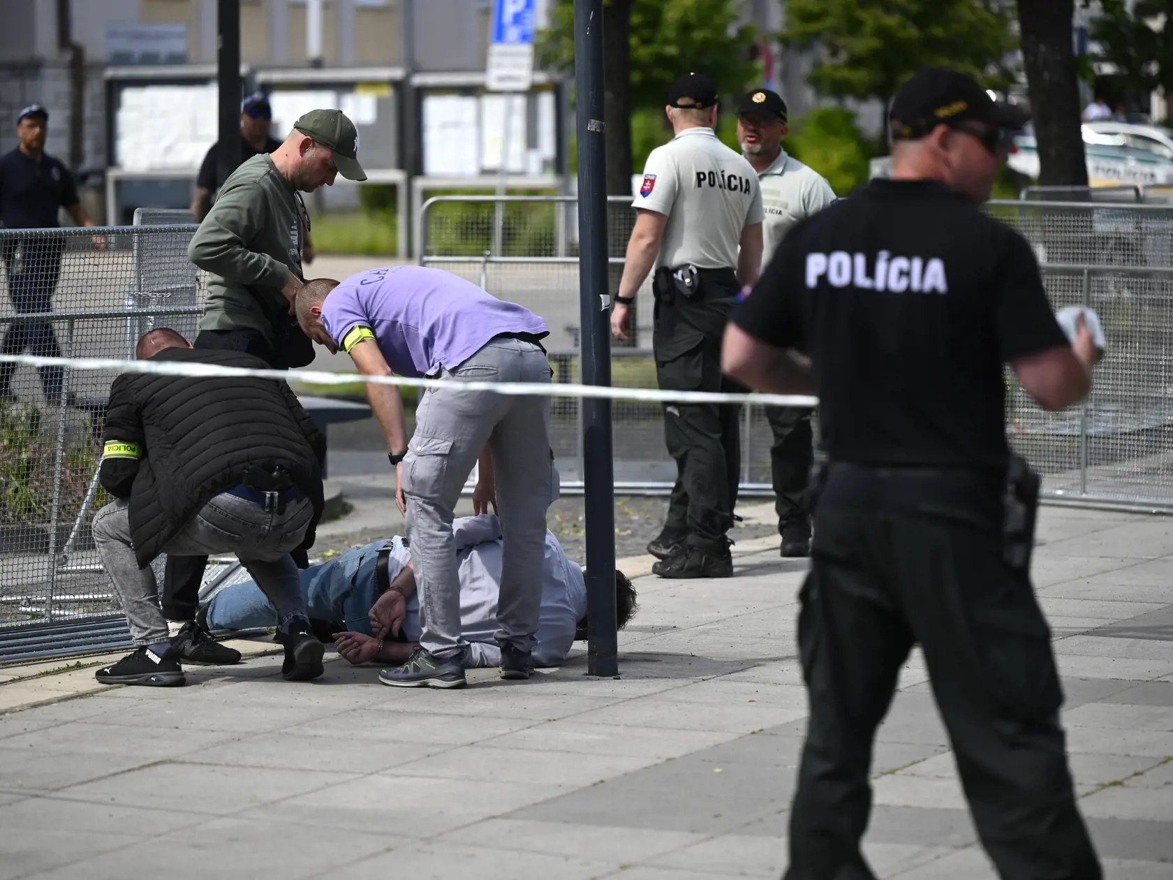 Na snímke policajti zatýkajú muža po streľbe na predsedu vlády Roberta Fica na výjazdovom rokovaní vlády v Handlovej v okrese Prievidza v stredu 15. mája 2024. Fica v stredu po výjazdovom rokovaní vlády v Handlovej postrelili. Na mieste padlo niekoľko výstrelov, útočníka zadržali.