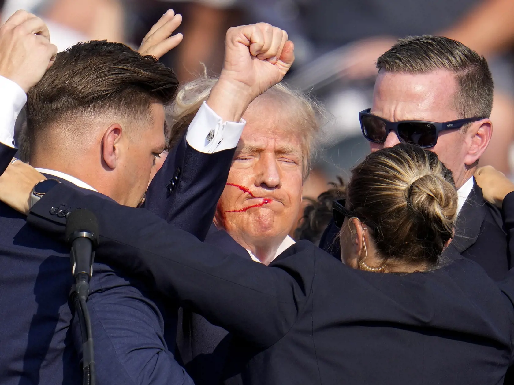 Republikánsky prezidentský kandidát Donald Trump (uporstred) reaguje pri odchode za pomoci ochrankárov z predvolebného mítingu v meste Butler v americkom štáte Pensylvánia 13. júla 2024. Trump potvrdil, že v sobotu na mítingu v Pensylvánii ho zasiahla guľka. Tá mu prestrelila hornú časť pravého ucha. Bývalý americký prezident sa vyjadril na sociálnej sieti, informuje TASR.