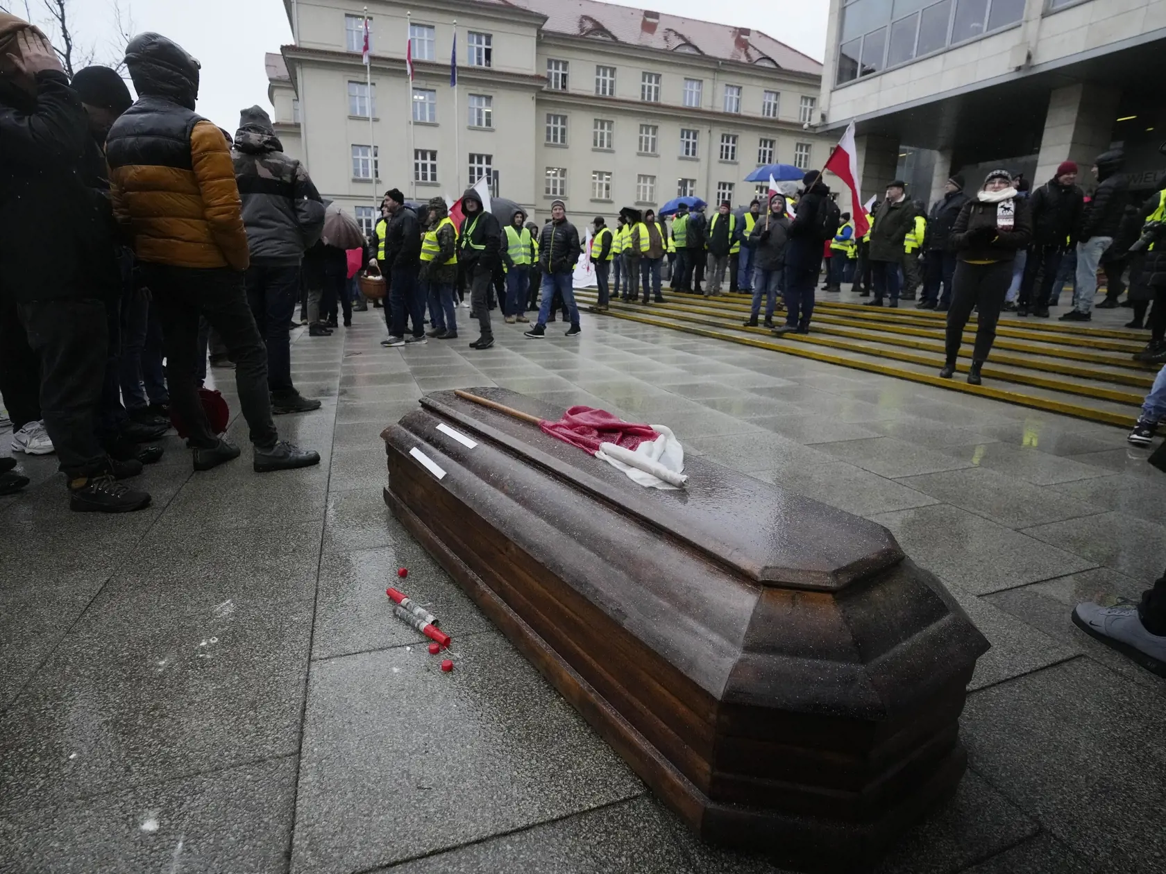 Poľskí farmári kladú rakvu s poľskou vlajkou symbolizujúcu stav poľského poľnohospodárstva pred úradnú budovu počas protestu v meste Poznaň na západe Poľska v piatok 9. februára 2024.