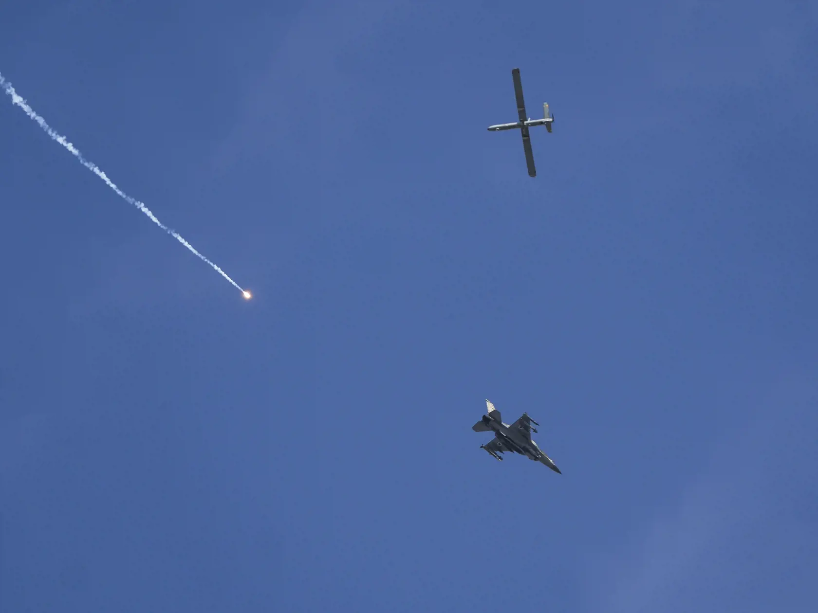 Izraelská stíhačka (dole) vypúšťa plamene a lietajúci dron (hore) čo je viditeľné z Rafahu, na juhu pásma Gazy 28. mája 2024 počas izraelskej pozemnej a leteckej ofenzívy. Izrael v noci na utorok opätovne útočil na oblasť okolo mesta Rafah na juhu Pásma Gazy a izraelské tanky prenikli do centra tohto mesta.