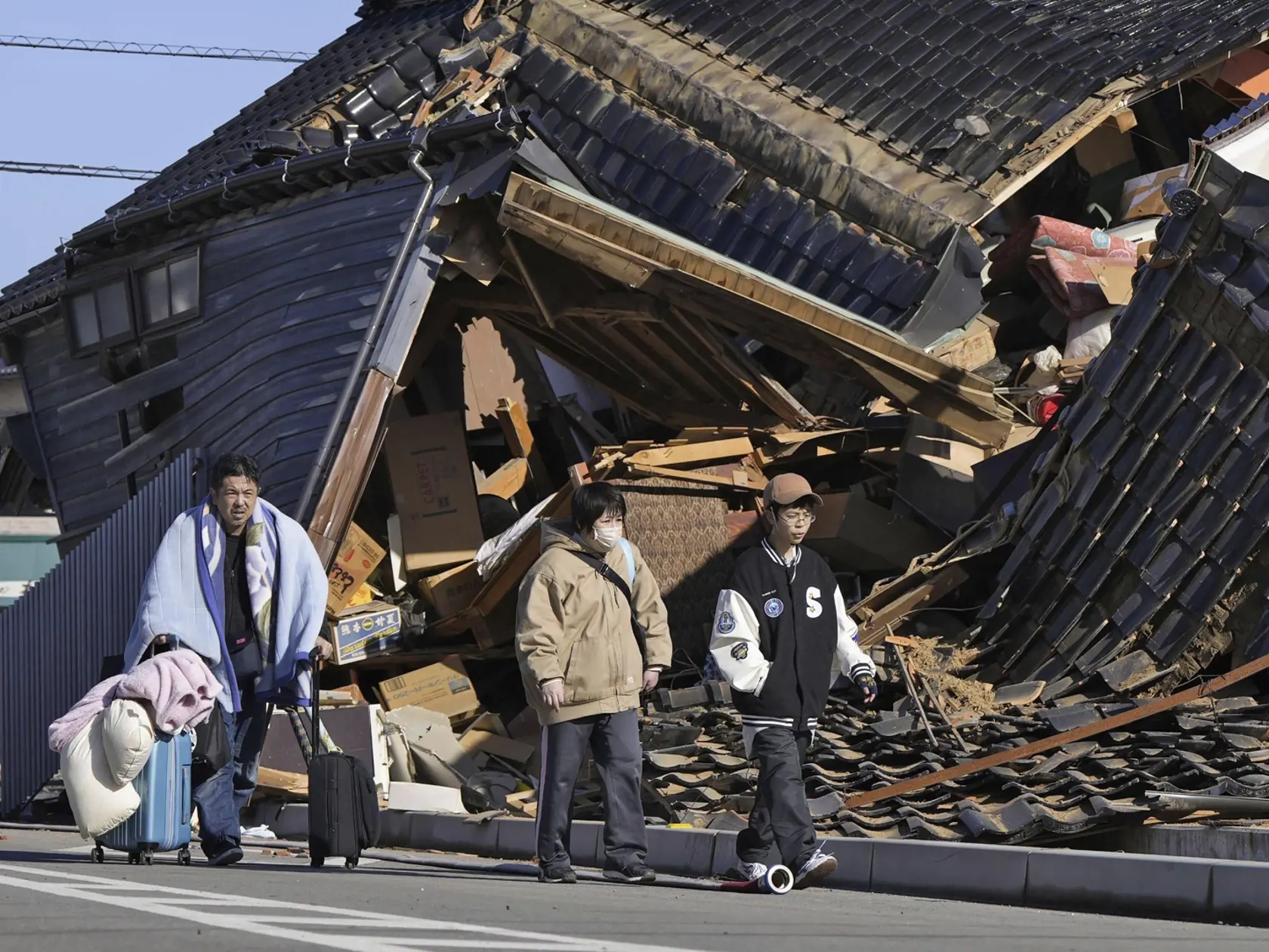 Na snímke muž nesie svoje veci okolo zrúteného domu po zemetrasení v prístavnom meste Wadžima v japonskej prefektúre Išikawa 2. januára 2024.