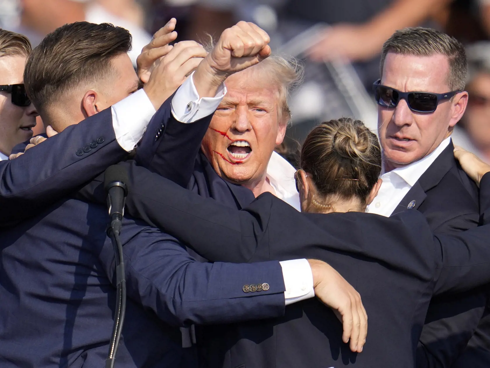 Republikánsky prezidentský kandidát Donald Trump (uprostred) reaguje pri odchode za pomoci ochrankárov z predvolebného mítingu v meste Butler v americkom štáte Pensylvánia 13. júla 2024. Trump potvrdil, že v sobotu na mítingu v Pensylvánii ho zasiahla guľka. Tá mu prestrelila hornú časť pravého ucha. Bývalý americký prezident sa vyjadril na sociálnej sieti, informuje TASR.