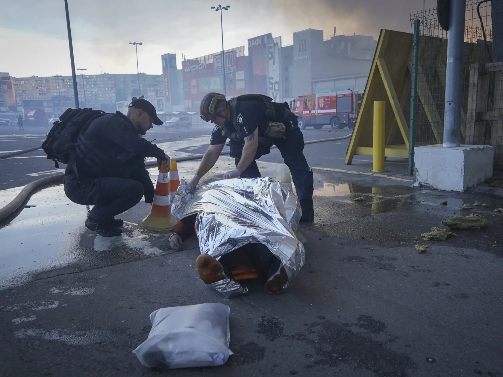 Policajti prikrývajú telo obete po tom, čo dve ruské navádzané bomby zasiahli hypermarket Epicentr v meste Charkov na severovýchode Ukrajiny v sobotu 25. mája 2024.