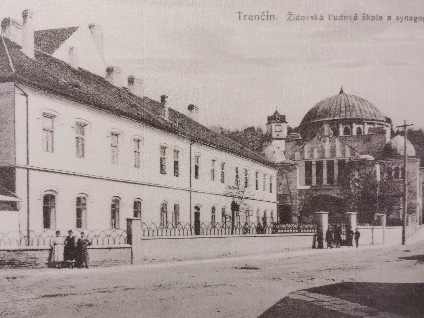 V popredí židovská ľudová škola, vzadu synagóga.