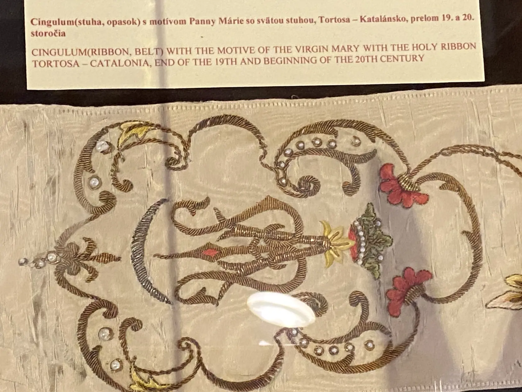 Detail výšivky v kráľovským erbom na opasku, ktoré nosila princezná Izabela v tehotenstve s motívom Panny Márie, pôvod Katalánsko z prelomu 19. a 20. storočia.
