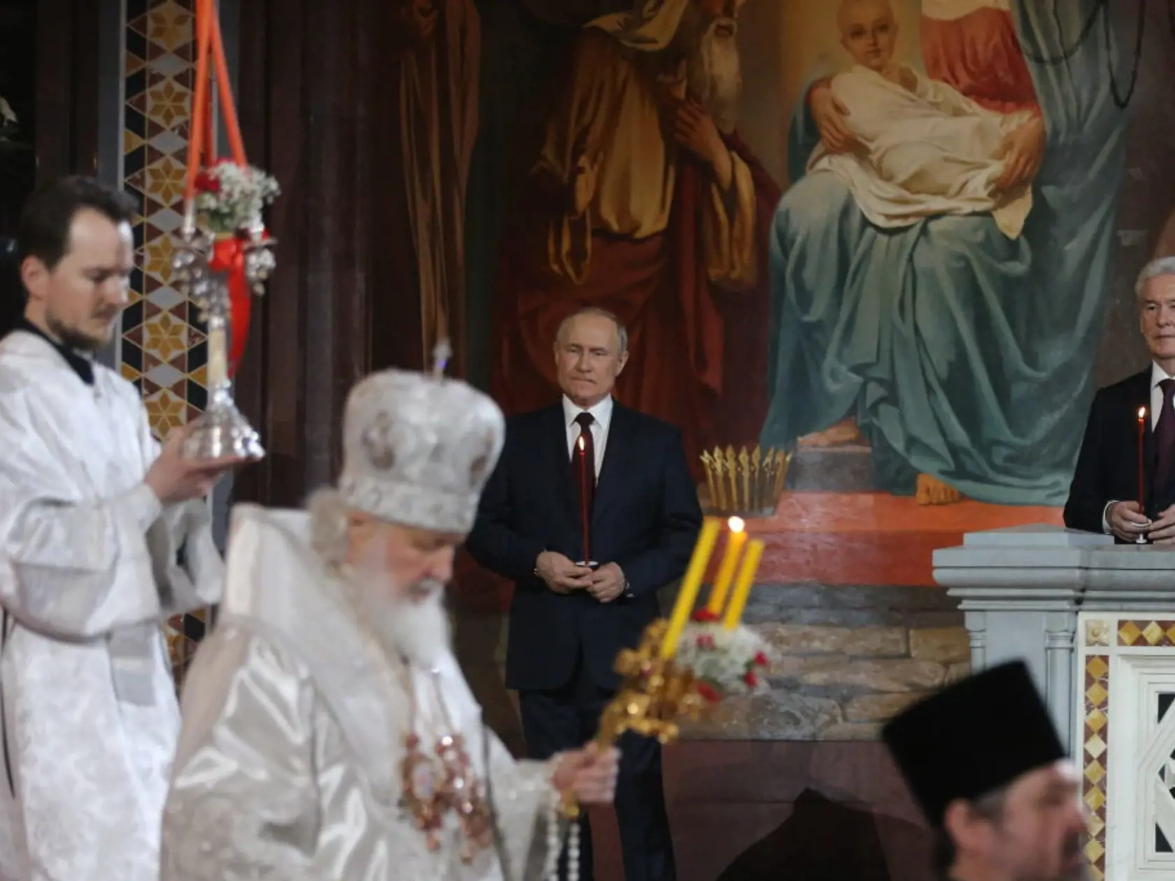 Putin oblečený v slávnostnom tmavomodrom obleku, bielej košeli a tmavofialovej kravate držal počas slávnostnej liturgie v ruke zapálenú sviecu a opakovane sa prežehnával