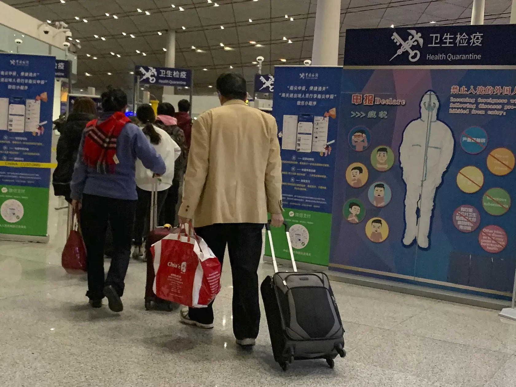Na snímke cestujúci kráčajú okolo kontrolného stanovišťa zdravotného stavu na letisku v Pekingu.