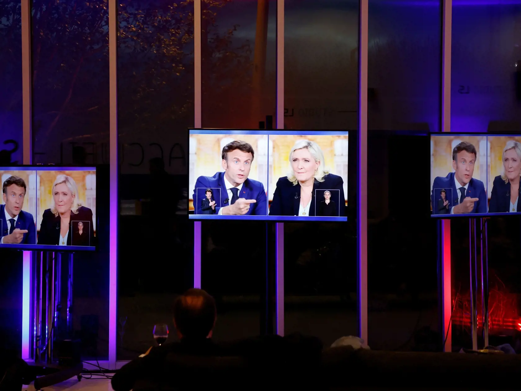 Ľudia sledujú francúzskeho prezidenta a centristického prezidentského kandidáta Emmanuela Macrona (vľavo) a francúzsku krajne pravicovú líderku a prezidentskú kandidátku Marine Le Penovú počas predvolebnej televíznej debaty v La Plaine-Saint-Denis pri Paríži 20. apríla 2022.