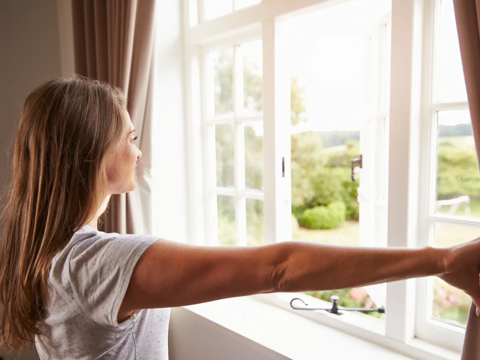 Woman,Standing,By,Bedroom,Window,And,Opening,Curtains