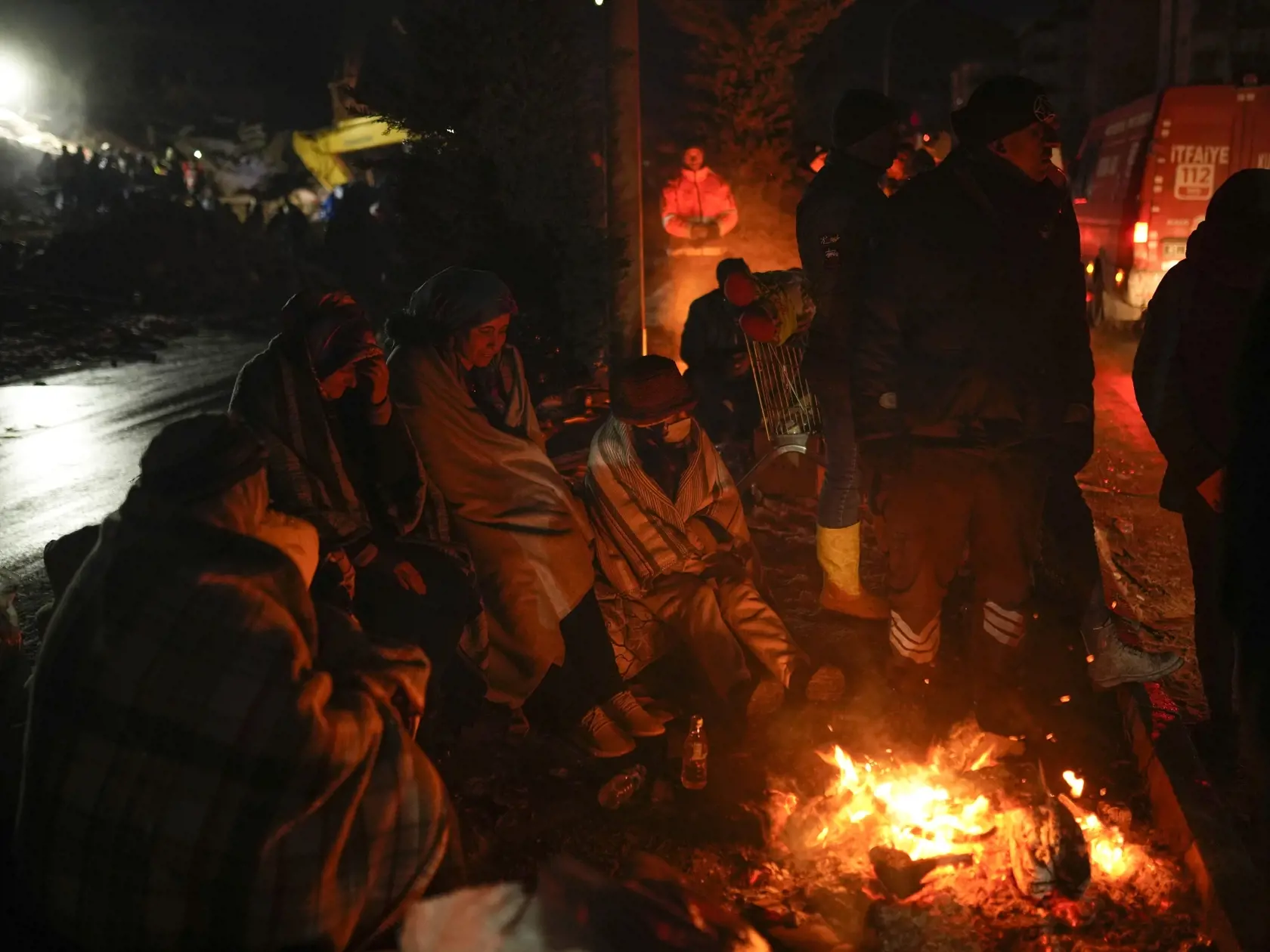 KK47 Elbistan - Ľudia sa zohrievajú pri ohni pred zničeným domom, zatiaľ čo záchranné tímy pátrajú po ľuďoch v tureckom meste Elbistan 8. februára 2023.