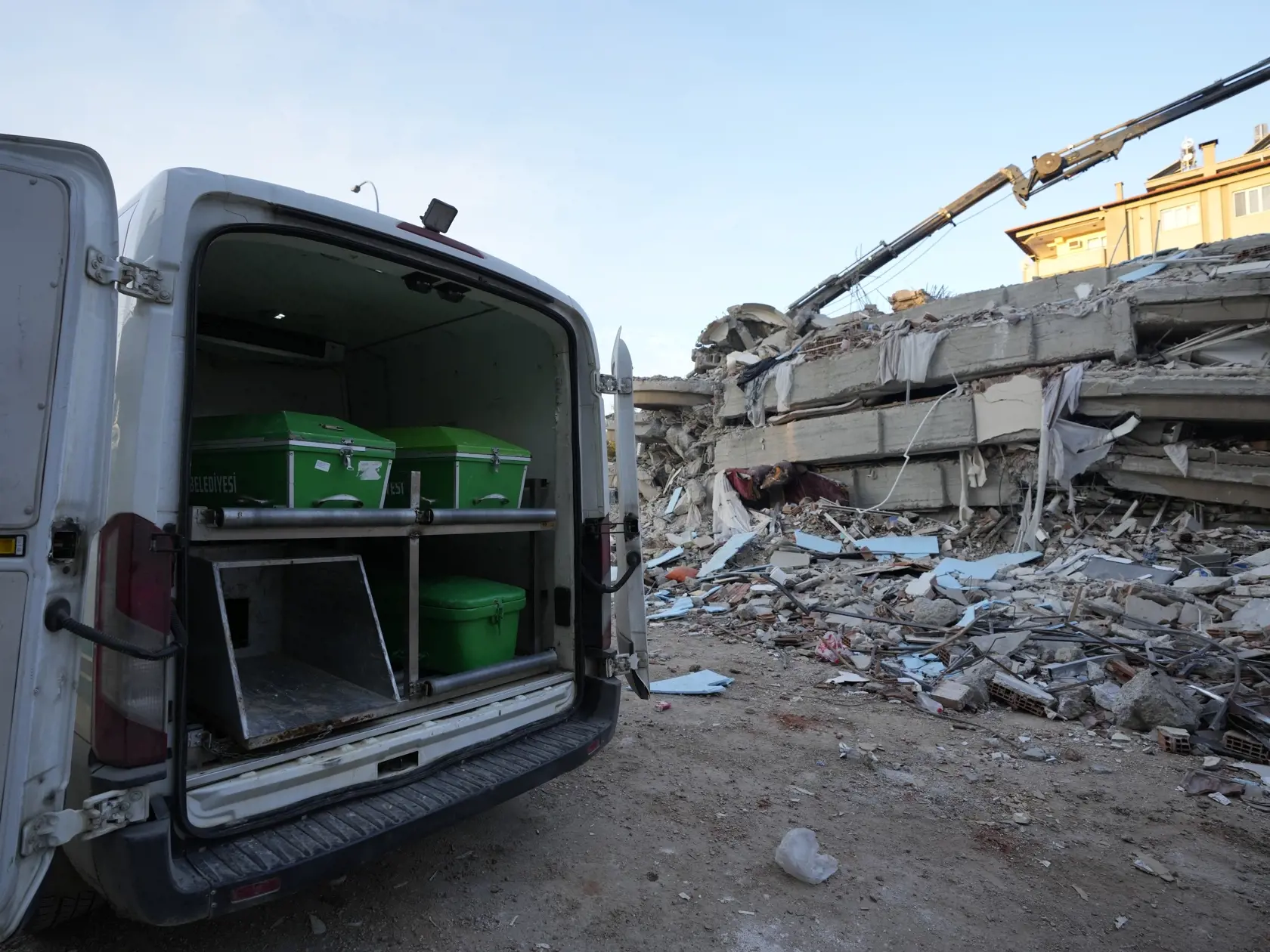 WA 28 Gaziantep - Dodávka s rakvami obetí zemetrasenia parkuje pri zrútenej budove v meste Gaziantep na juhovýchode Turecka v stredu 8. februára 2023.