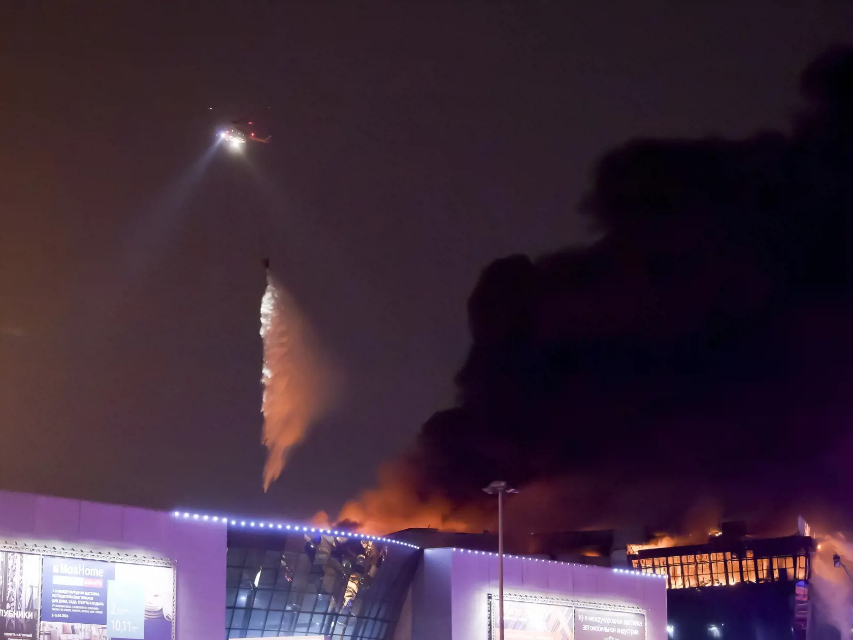 JB 19 Moskva - Vrtuľník bojuje s masívnym plameňom nad horiacou budovou koncertnej sály Crocus City Hall v západnej časti Moskvy 22. marca 2024. Pri piatkovom útoku ozbrojencov na koncertnú halu na predmestí Moskvy zahynulo viac ako 60 ľudí, uviedol v sobotu ruský vyšetrovací výbor. Pôvodne uvádzaný počet obetí bol viac ako 40, informuje agentúra AFP s odvolaním sa na ruské tlačové agentúry. "Momentálne sa obhliadajú telá zosnulých. Predbežne sa zistilo, že pri teroristickom útoku zomrelo viac