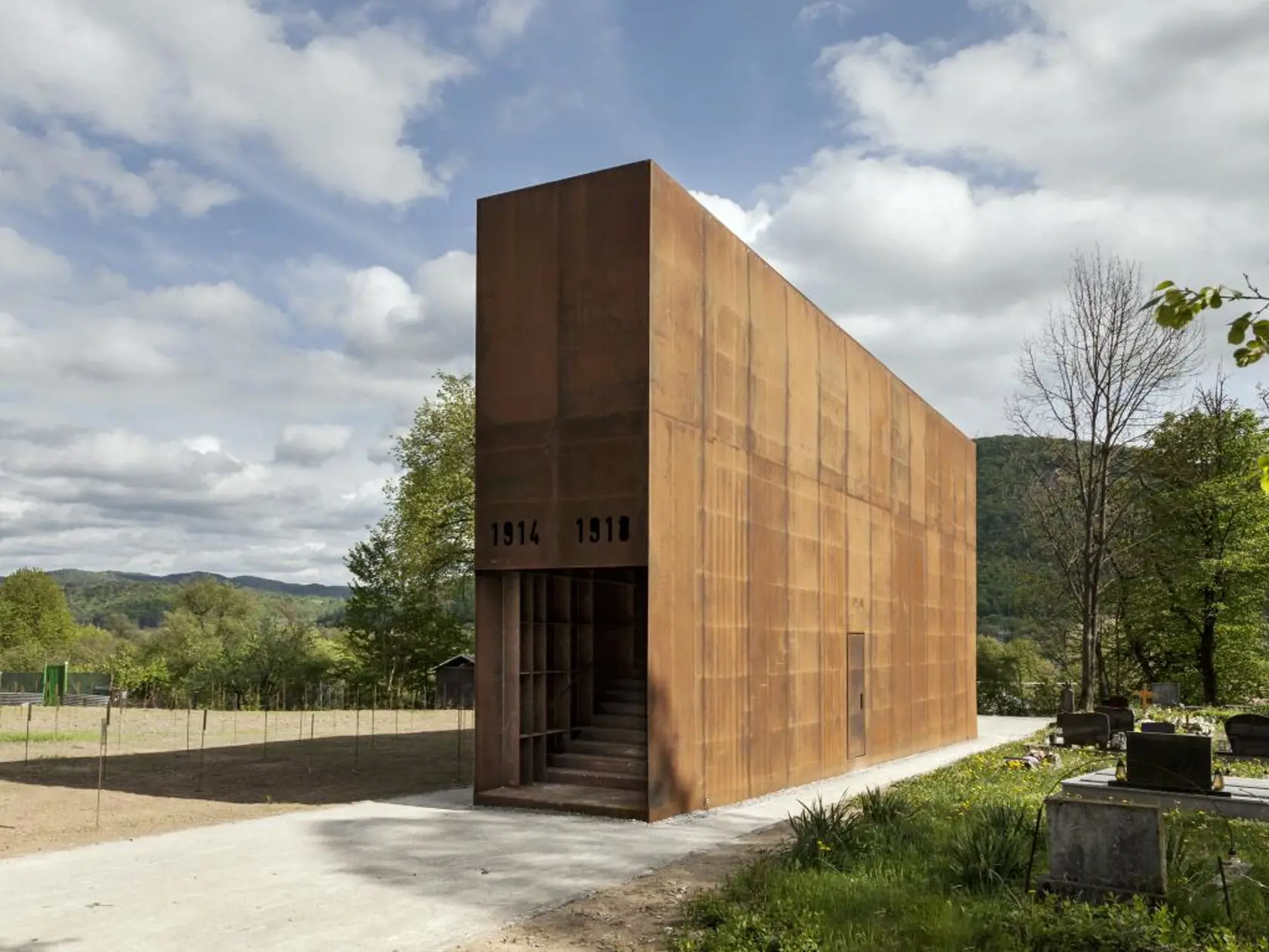 #MONUMENT MAJER:  Obnovu vojnového cintorína chápeme ako vizualizáciu priestoru zabúdania, vytláčania toho, čo by sme si mali pamätať. Cintorín bol v 50-tych rokoch opustený a pretnutý križovatkou ciest. Na centrálnej časti bola postavená v 90-tych rokoch budova autosalónu a zvyšok zmizol pod stromami a krami. Ústredným bodom obnovy je MONUMENT.