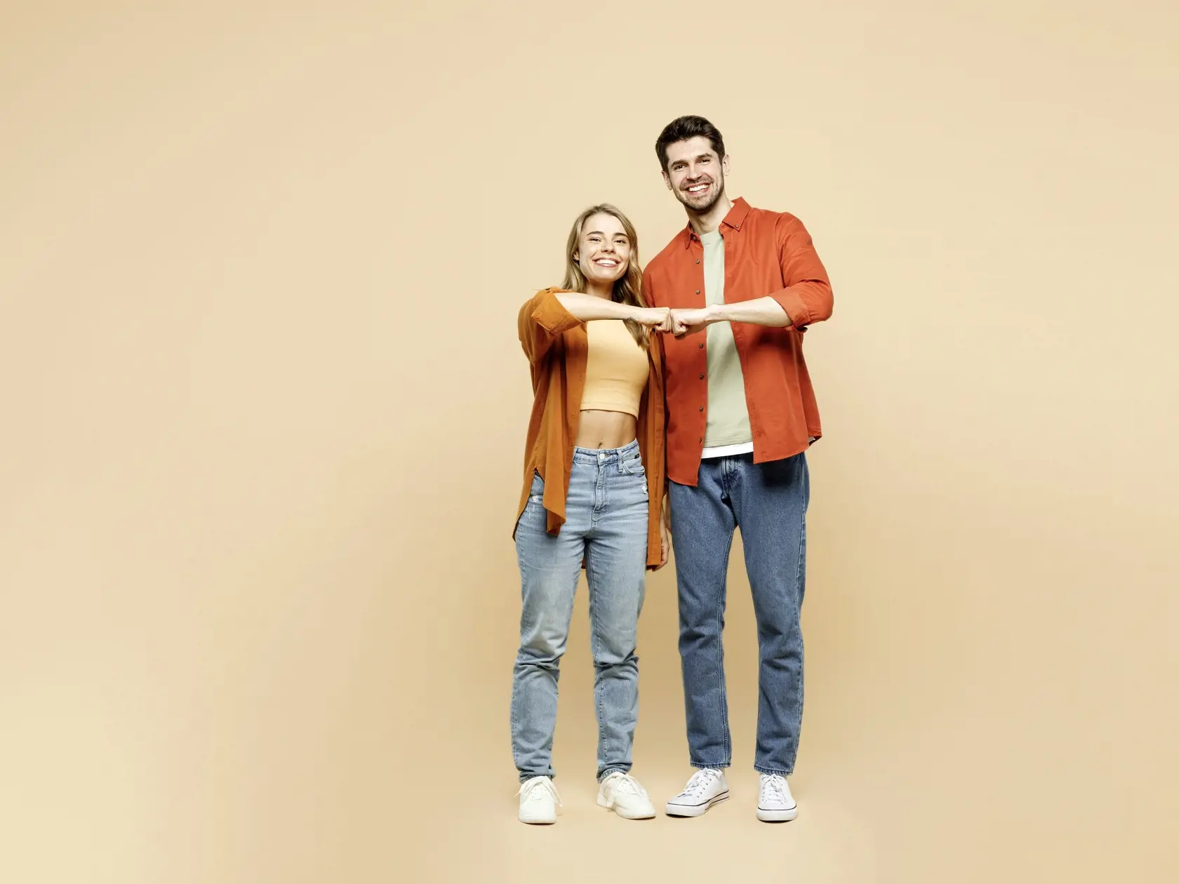 Full body smiling cheerful fun young couple two friends family man woman wear casual clothes together giving fist bump look camera isolated on pastel plain light beige color background studio portrait