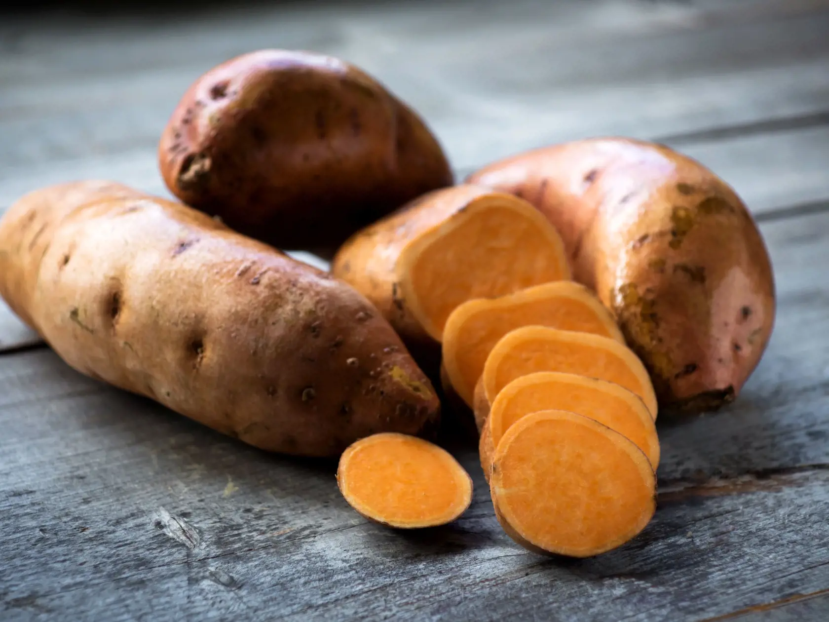 Raw sweet potatoes on wooden background closeup