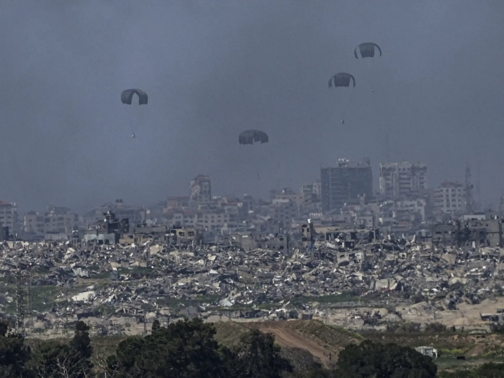 Padáky s humanitárnou pomocou sú vyhadzované na sever pásma Gazy, čo je viditeľné z juhu Izraela v stredu 13. marca 2024. Izraelská armáda bojuje s palestínskymi militantmi hnutia Hamas v pásme Gazy po útokoch Hamasu na Izrael 8. októbra.