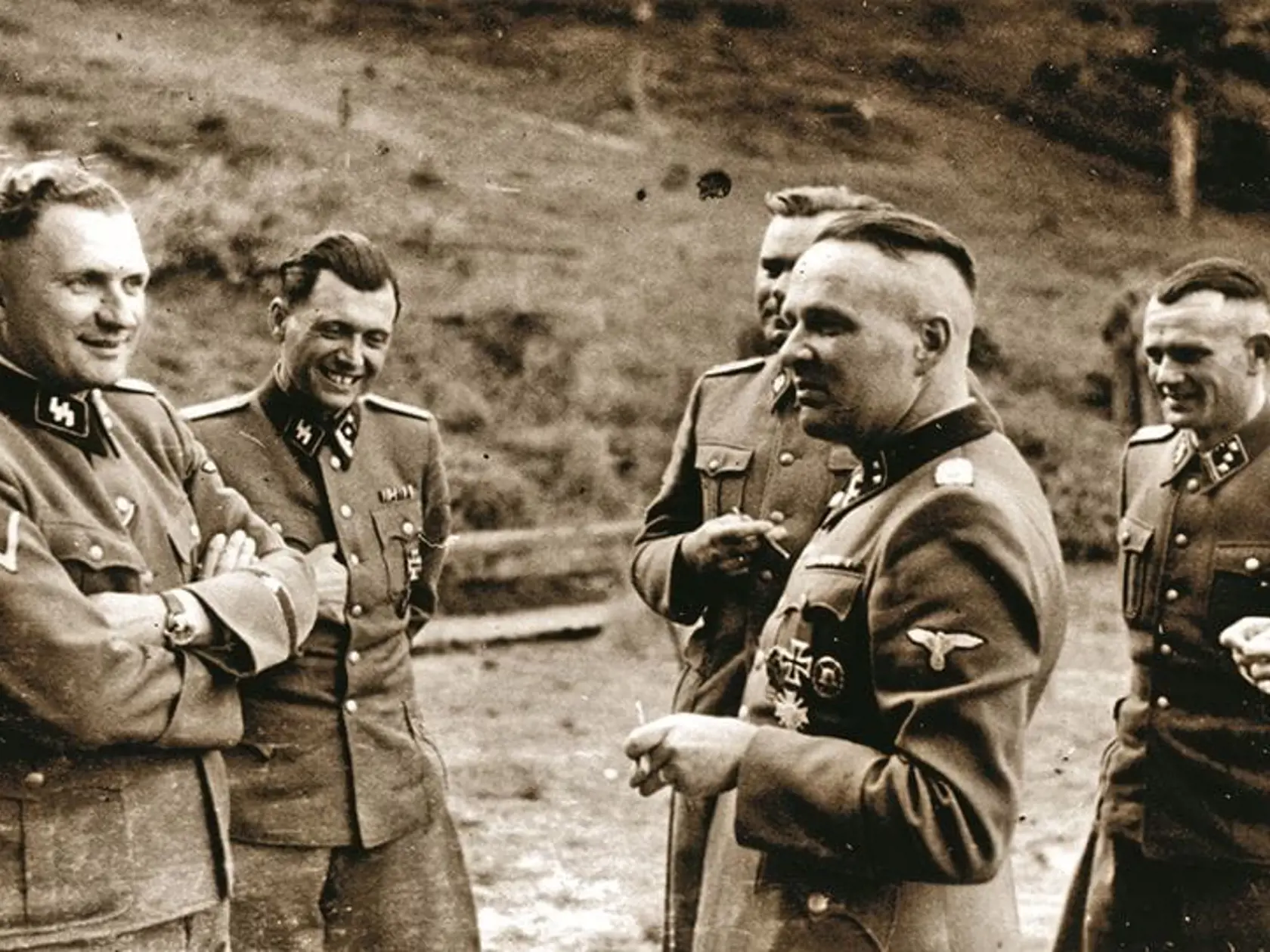 Josef Mengele: Poznávacie znaky druhého muža zľava - neárijský vzhľad, tmavé oči, hnedé vlasy, medzierka medzi zubami.