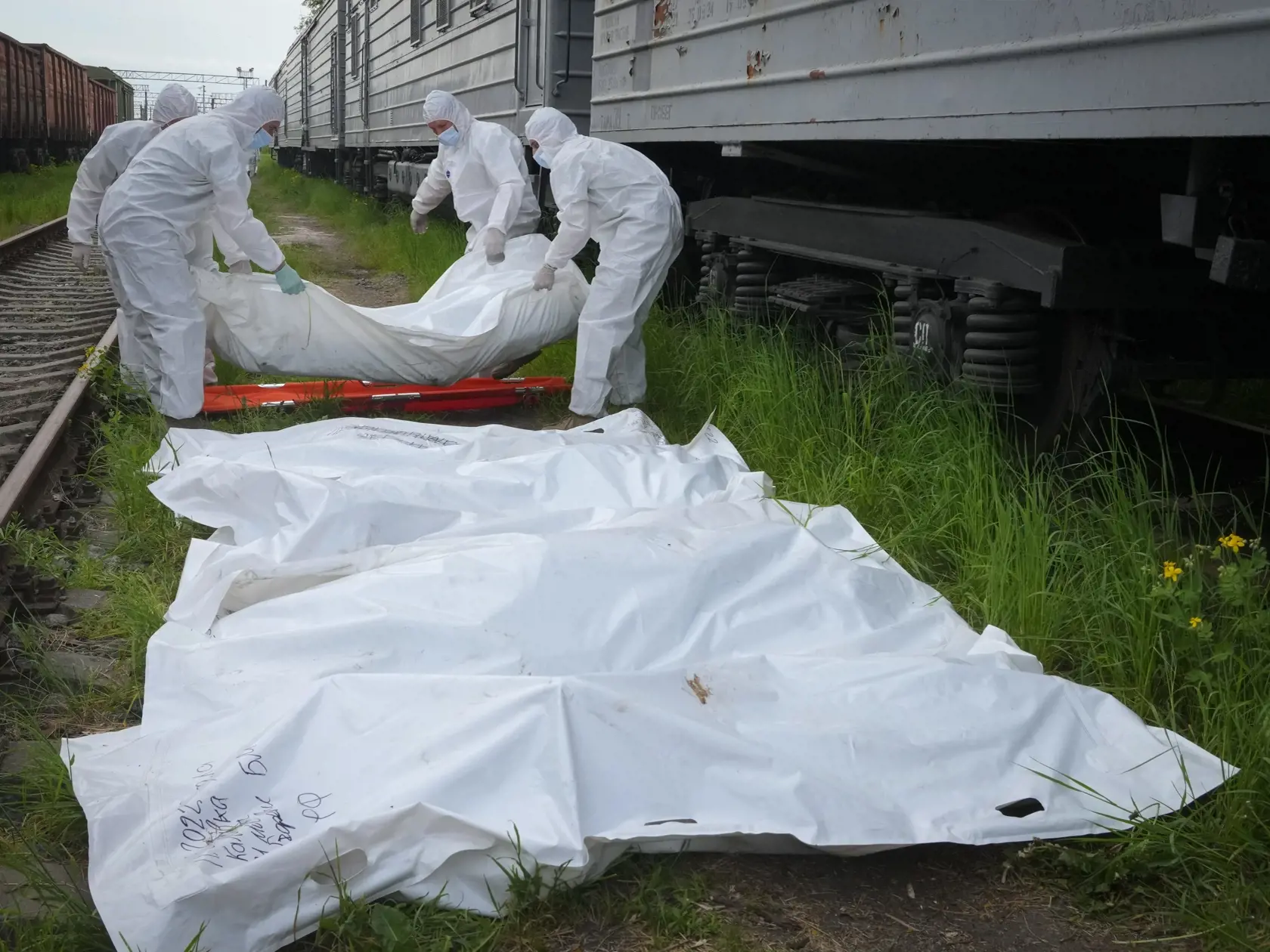 Ukrajinskí vojaci v špeciálnych ochranných odevoch nakladajú telá ruských vojakov do vlakového chladiarenského vozňa v Kyjeve počas 79. dňa ruskej invázie na Ukrajinu v piatok 13. mája 2022.