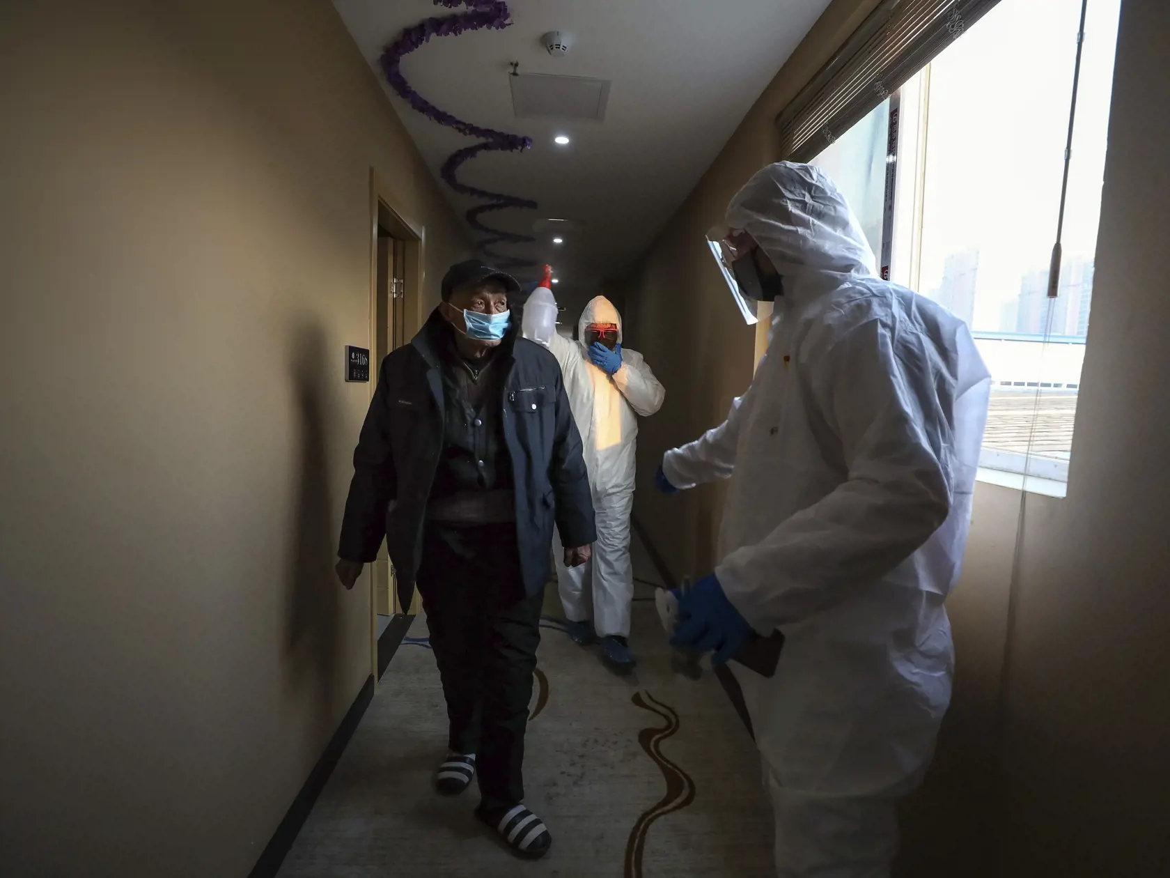 KK11 Wu-chan - Na snímke pracovníci v ochranných odevoch doprevádzajú muža v hoteli, ktorý slúži na lekársku izoláciu ľudí 3. februára 2020 v čínskom Wu-chane. Počet potvrdených úmrtí v dôsledku nakazenia novým koronavírusom 2019-nCoV v Číne v utorok stúpol na 425. Celkový počet infikovaných stúpol na vyše 20.400 osôb. V oblasti mesta Wu-chan v provincii Chu-pej, považovaného za epicentrum šírenia vírusu, boli už predtým zavedené karanténne zóny s obmedzeným pohybom obyvateľstva, v ktorých žije 