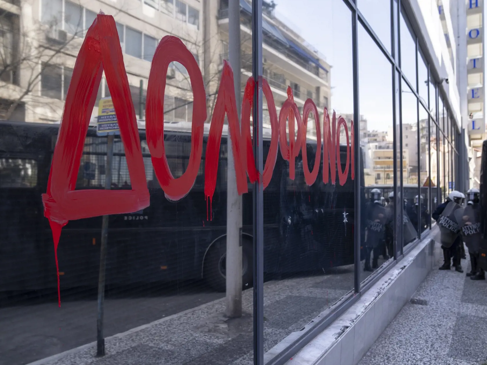 Grécke slovo "vrahovia" je namaľované na skle sídla železničnej spoločnosti Hellenic Train, zatiaľčo príslušníci gréckych poriadkových síl hliadkujú počas protestného zhromaždenia univerzitných študentov v Aténach 3. marca 2023. Stovky protestujúcich si pred gréckym parlamentom v piatok minútou ticha uctili pamiatku obetí utorkovej tragickej čelnej zrážky dvoch vlakov, informuje agentúra AFP, od ktorej TASR správu prevzala.