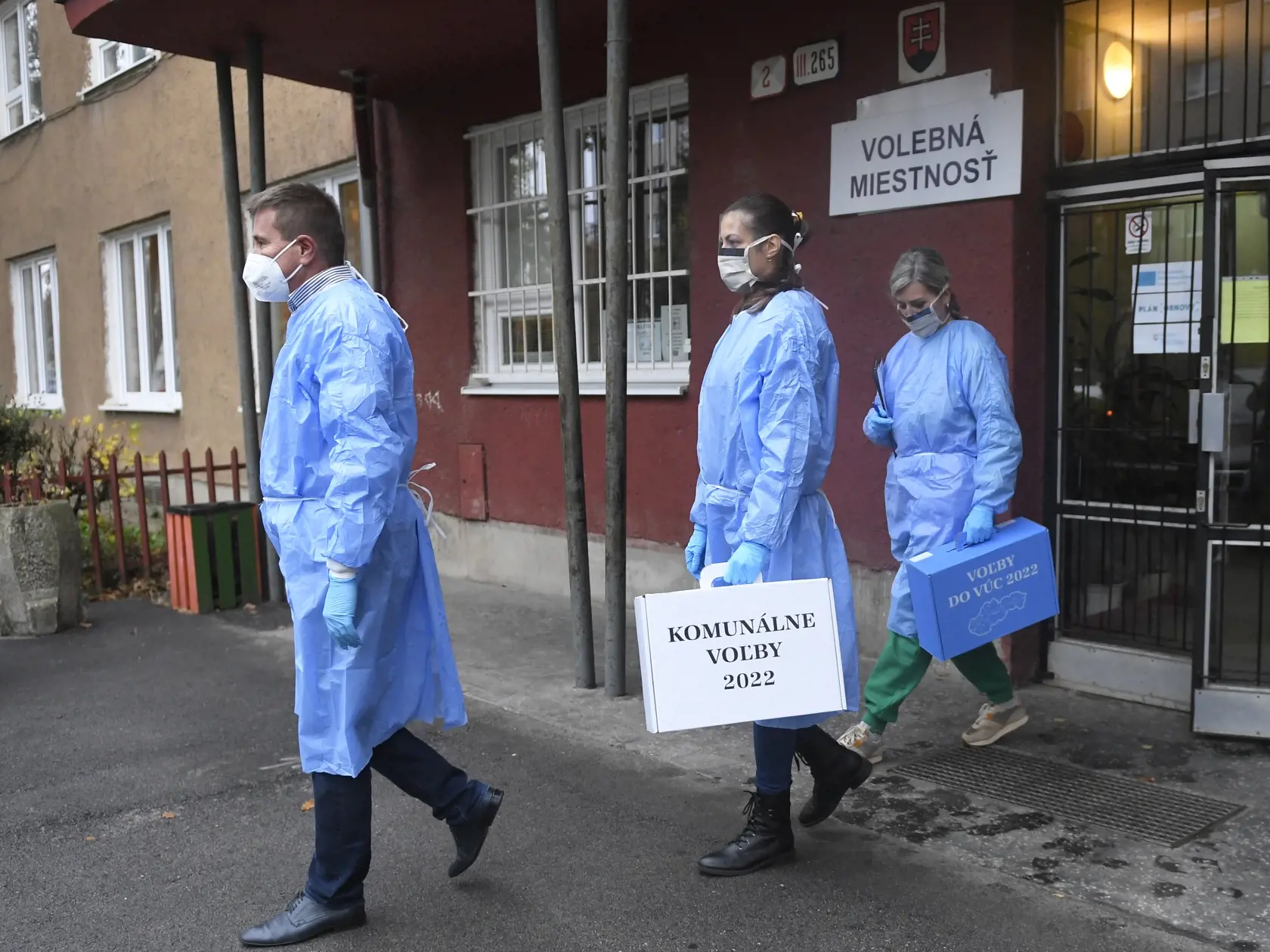 Na Slovensku sa v sobotu o siedmej hodine ráno začali historicky prvé spojené voľby do orgánov samosprávy obcí a do orgánov samosprávnych krajov. Na snímke členovia špeciálnej volebnej komisie vybavení osobnými ochrannými pracovnými prostriedkami kráčajú so špeciálnymi volebnými schránkami za voličom v izolácii pre Covid-19 do domácnosti v Košiciach v mestskej časti Sever 29. októbra 2022. FOTO TASR – František Iván
