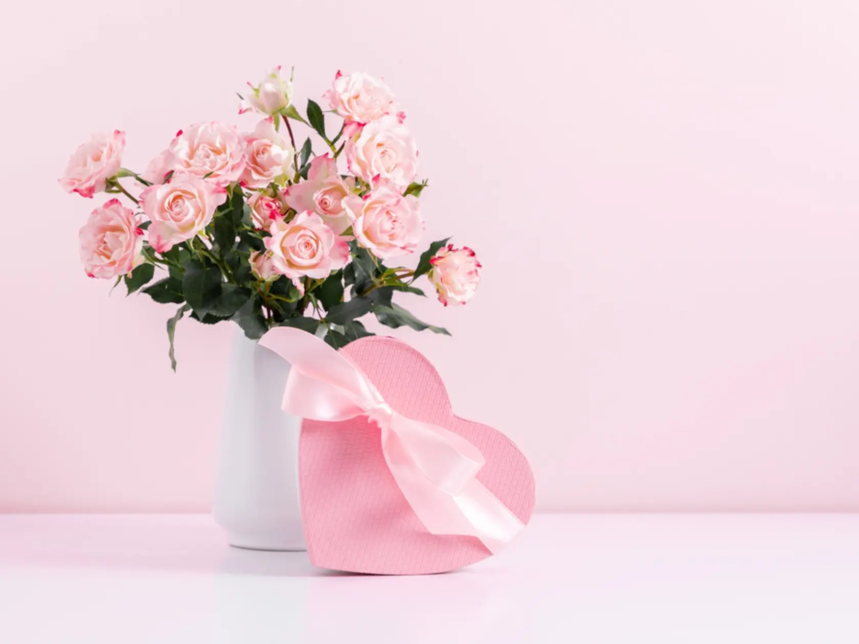 Beautiful bouquet flowers pink roses in vase and  gift box with satin bow on pastel pink background table. Birthday, Wedding, Mother's Day, Valentine's day, Women's Day. Front view