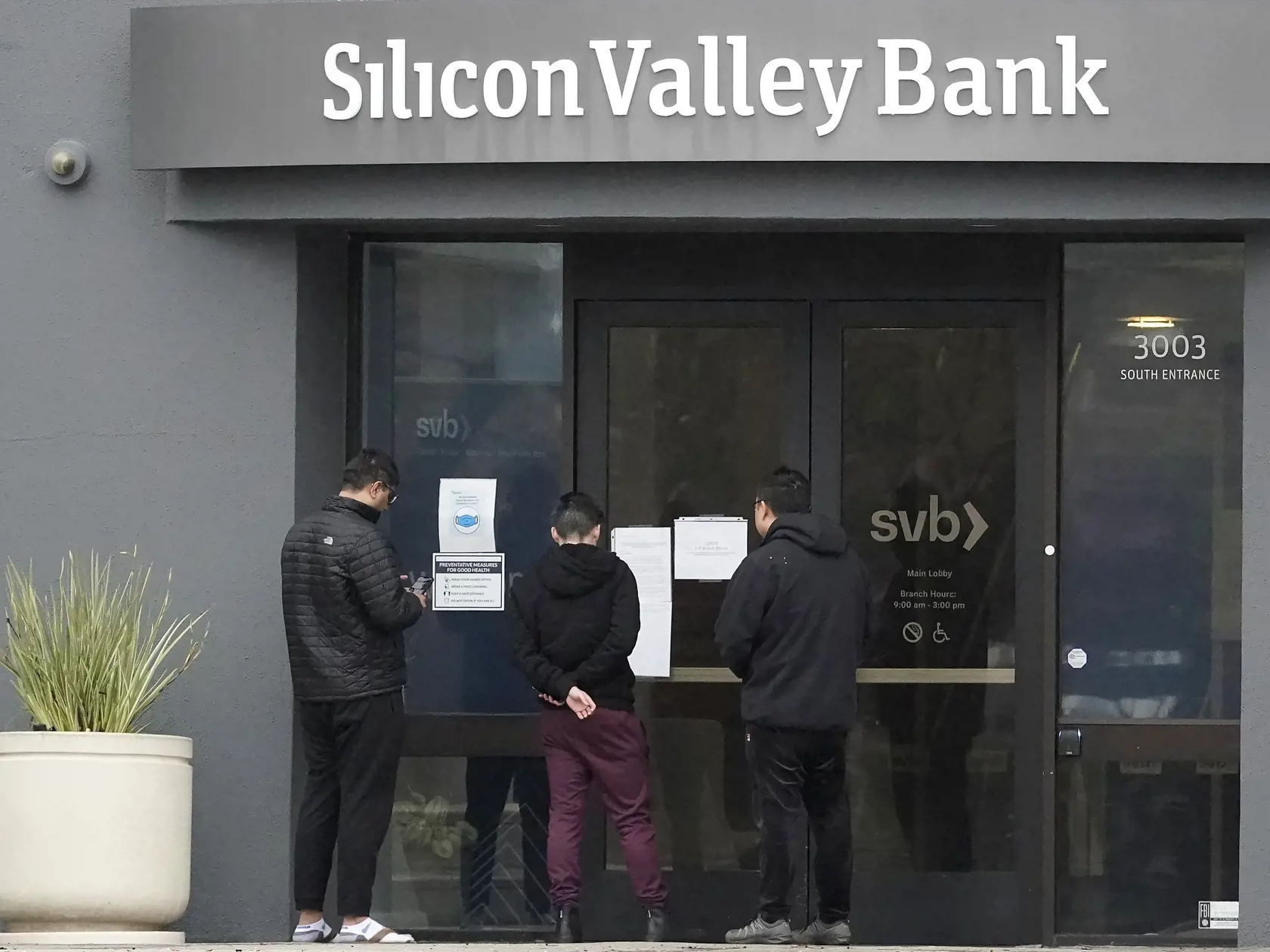 WA 40 Santa Clara - Ľudia si čítajú oznam pred vchodom do banky Silicon Valley Bank (SVB) v kalifornskej Santa Clare v piatok 10. marca 2023. Po skončení desaťročnej éry lacných peňazí sa v globálnom finančnom systéme objavujú trhliny. Niektorí investori sa tak obávajú "šírenia nákazy" vo finančnom sektore po kolapse banky Silicon Valley Bank (SVB) tento týždeň, ktorá sa špecializovala na technologické spoločnosti podporované rizikovým kapitálom. FOTO TASR/AP    

People look at signs posted out