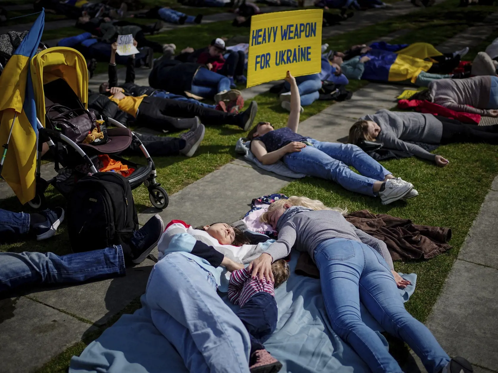 Berlín - Demonštranti ležia na zemi a protestujú pred úradom nemeckého kancelára Olafa Scholza proti vojne na Ukrajine v Berlíne v pondelok 25. apríla 2022. Demonštrantka drží transparent s nápisom "Ťažké zbrane pre Ukrajinu".