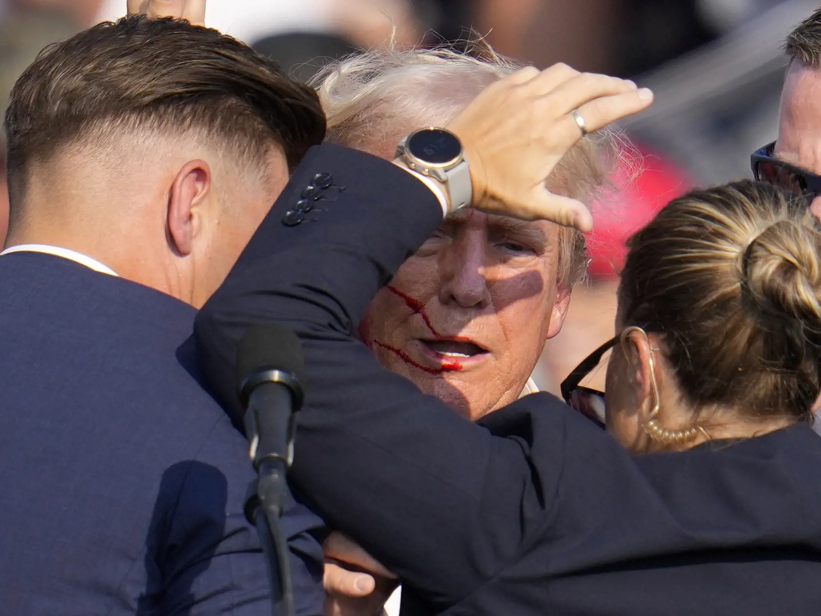Republikánsky prezidentský kandidát Donald Trump (uporstred) reaguje pri odchode za pomoci ochrankárov z predvolebného mítingu v meste Butler v americkom štáte Pensylvánia 13. júla 2024. Trump potvrdil, že v sobotu na mítingu v Pensylvánii ho zasiahla guľka. Tá mu prestrelila hornú časť pravého ucha.