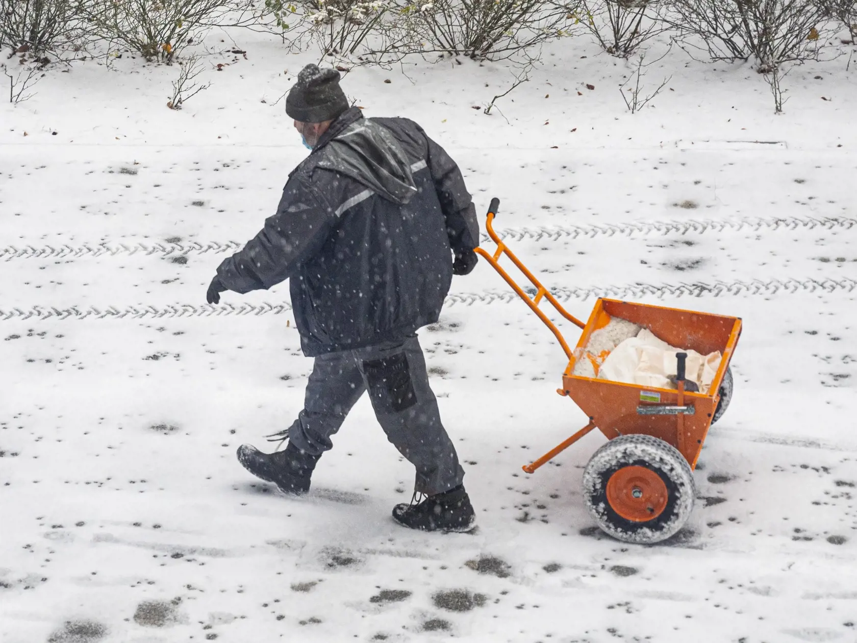 Muž posýpa zasnežený chodník počas ranného sneženia v Bratislave 3. decembra 2020.  FOTO TASR - Michal Svítok